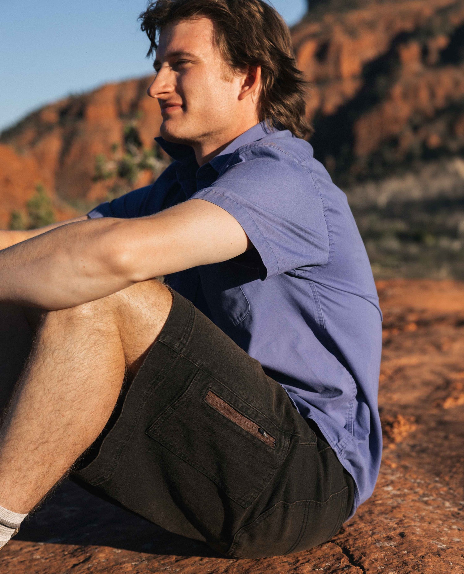 Man sitting on a rock with a scenic background of red cliffs.