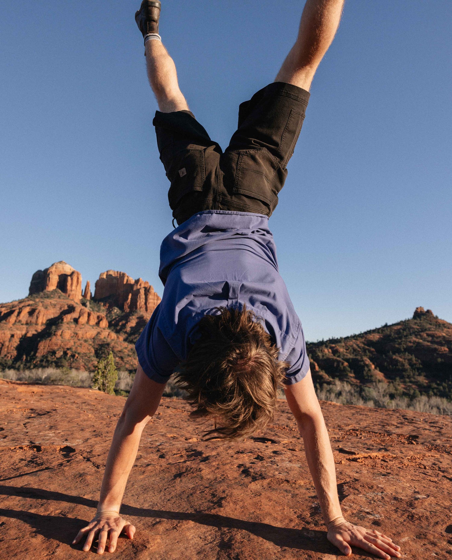 Person doing a handstand on a rocky landscape with red rock formations in the background