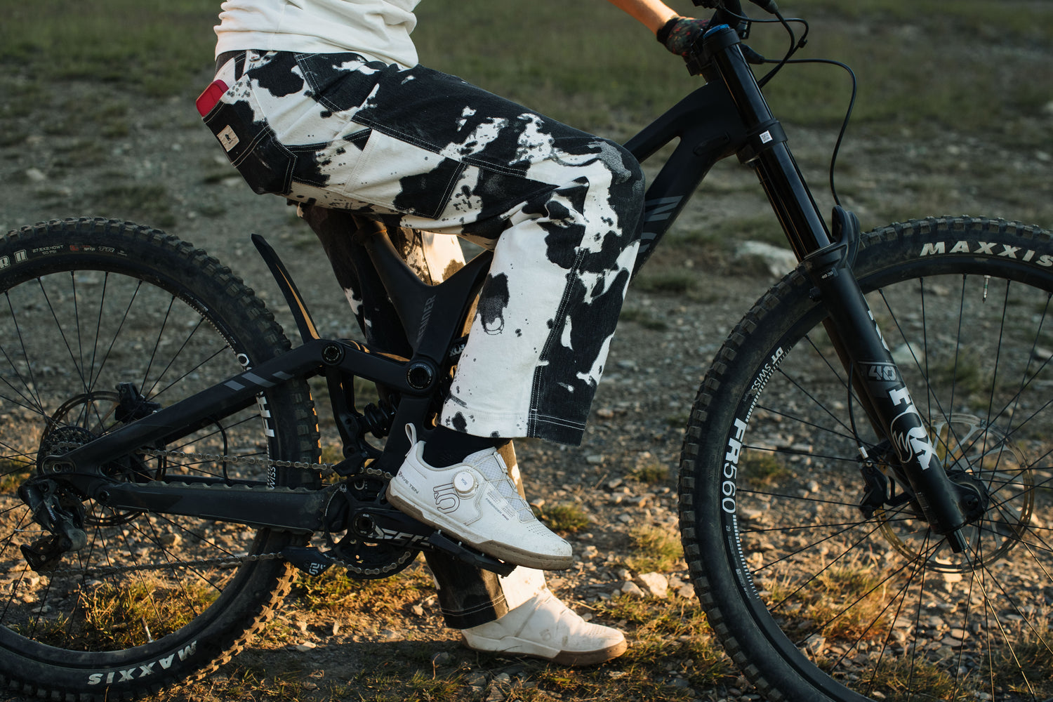 Person wearing black and white patterned pants riding a bicycle on a grassy path.