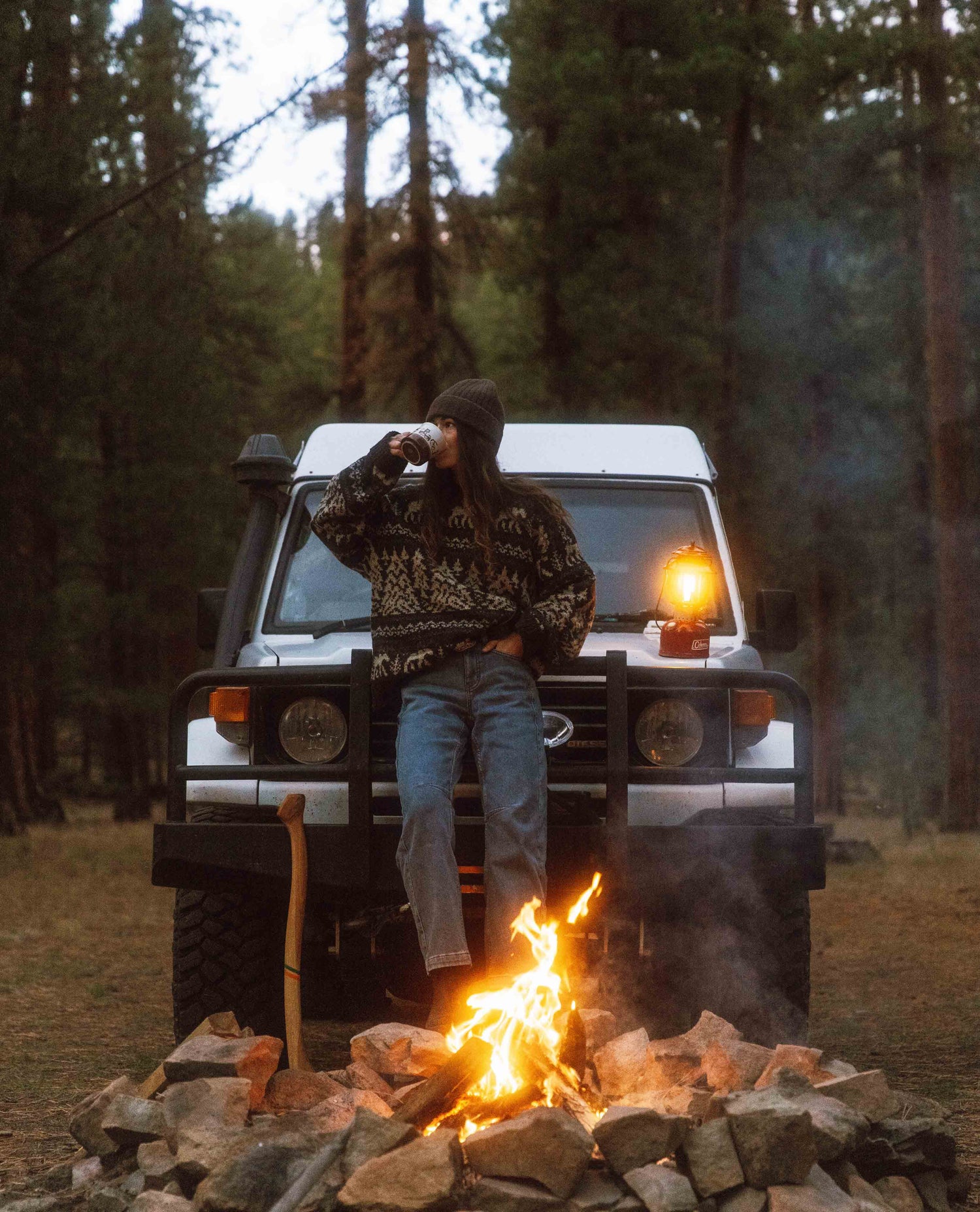 Person sitting on a jeep next to a campfire in a forest