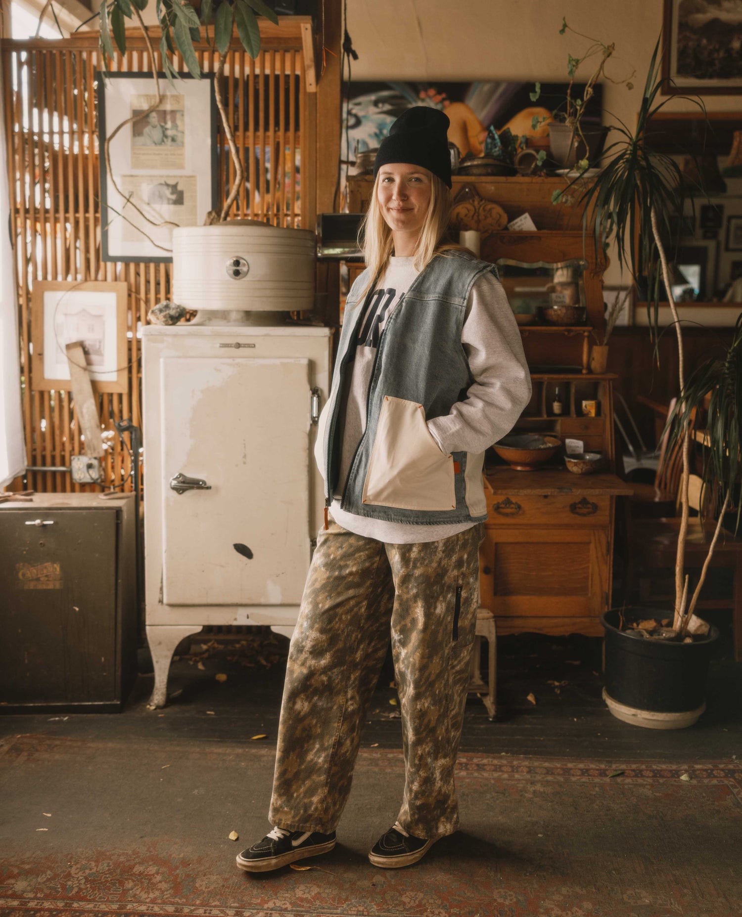 Person wearing a black hat and casual outfit standing in a room with vintage furniture and decor.