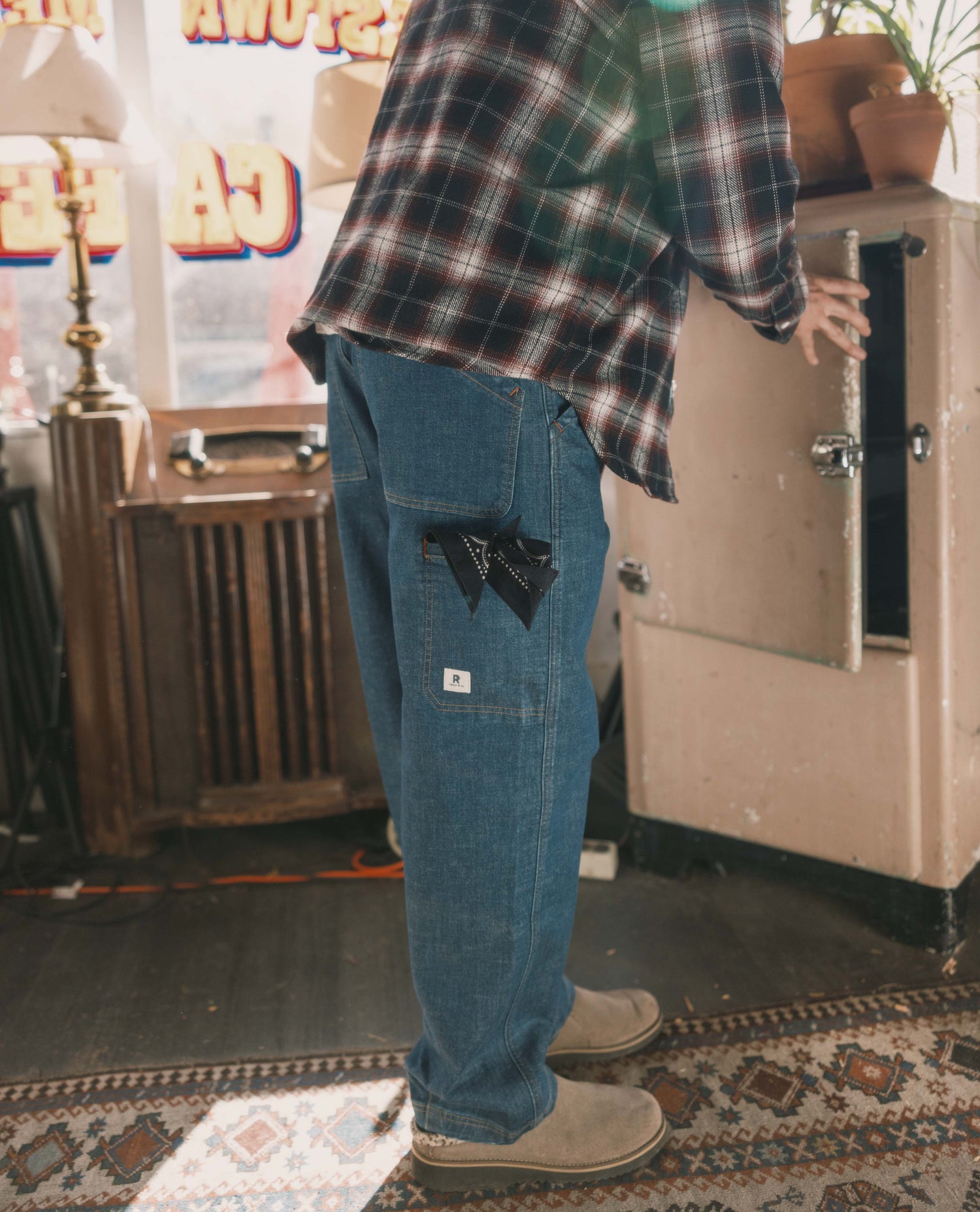 Person wearing a plaid shirt and blue jeans in an indoor setting with vintage decor.
