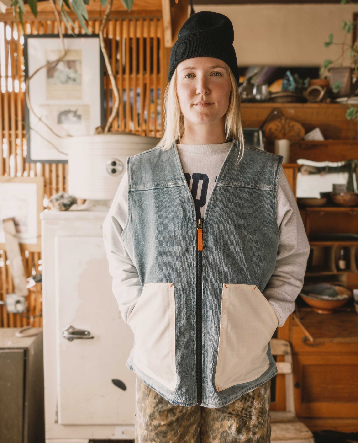 Person wearing a denim vest and black beanie in a rustic indoor setting