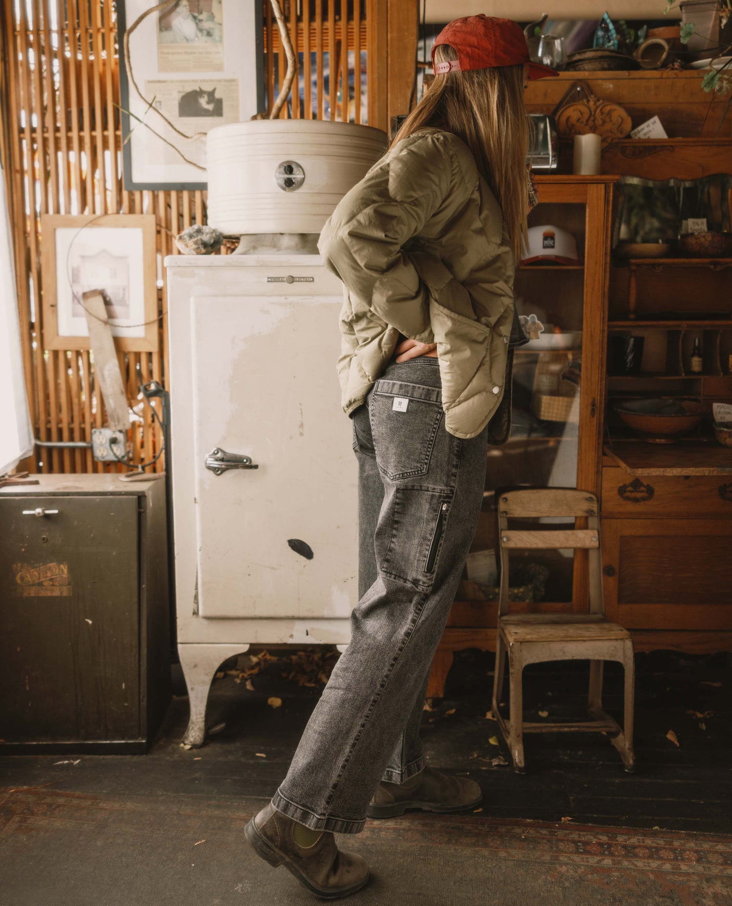 Person wearing a green jacket and red beanie in a rustic indoor setting with wooden furniture and a white refrigerator.
