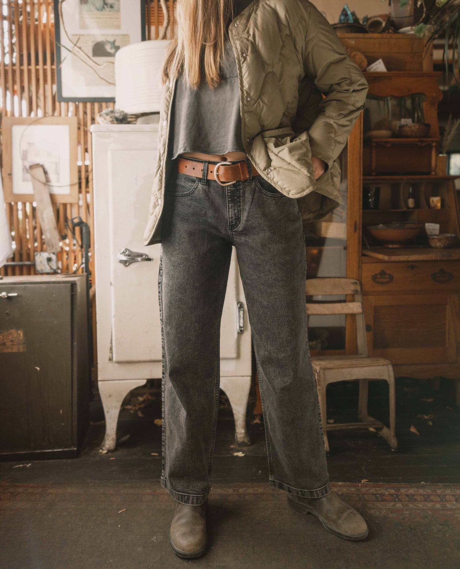 Person wearing a green jacket and dark jeans standing in a rustic indoor setting.