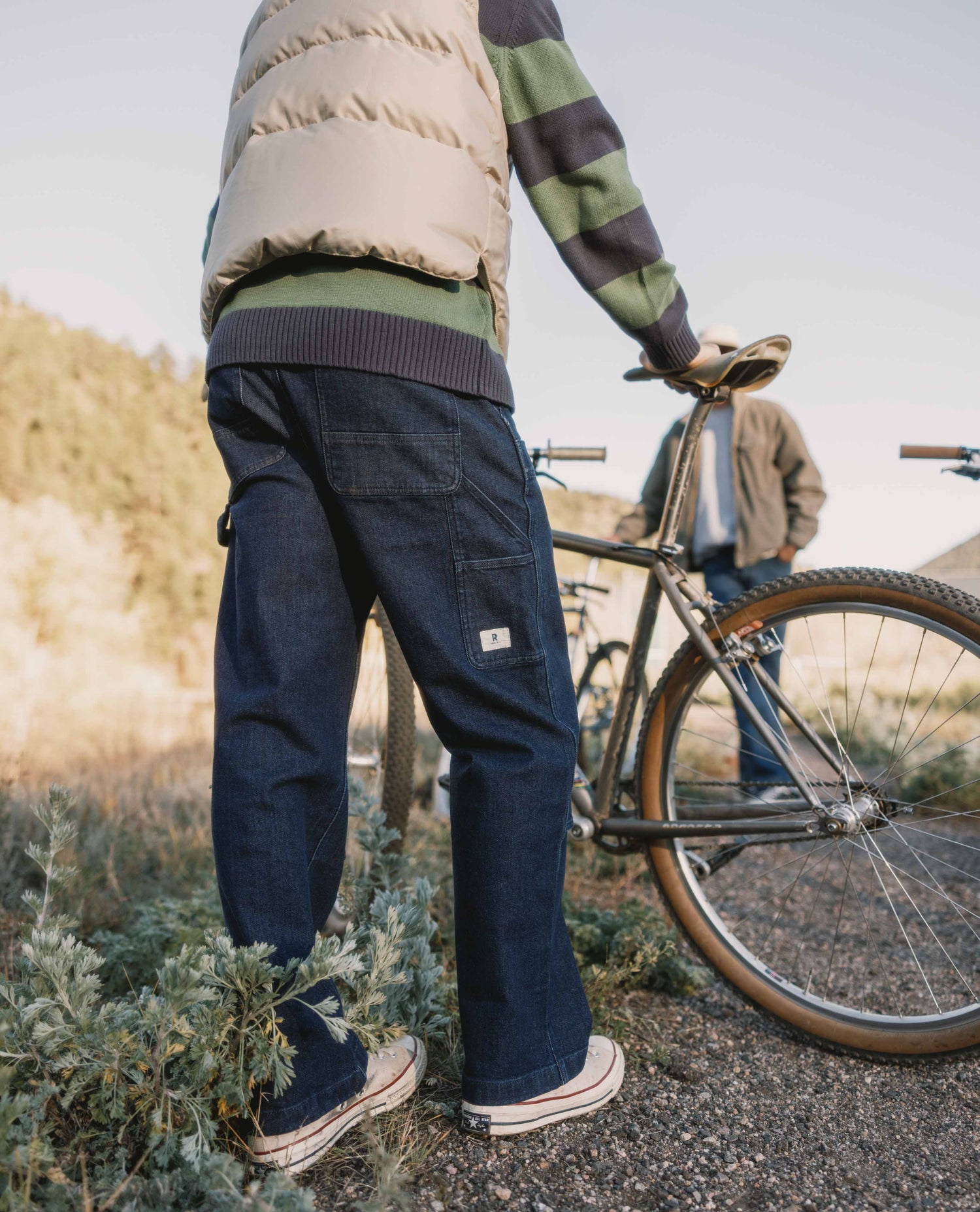 Person wearing navy pants and a striped sweater, standing next to a bicycle in a natural setting.