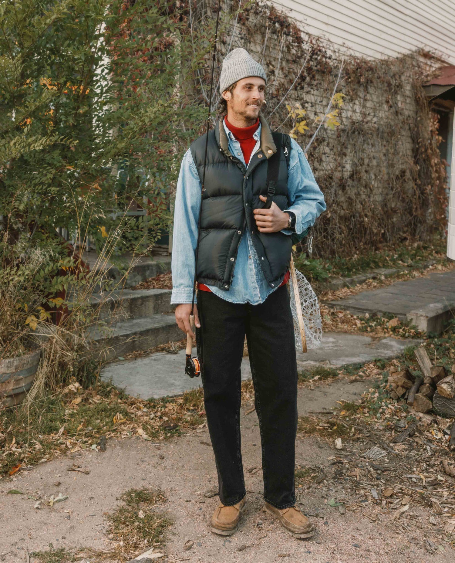 Man standing outdoors wearing a vest, light blue shirt, and dark pants.