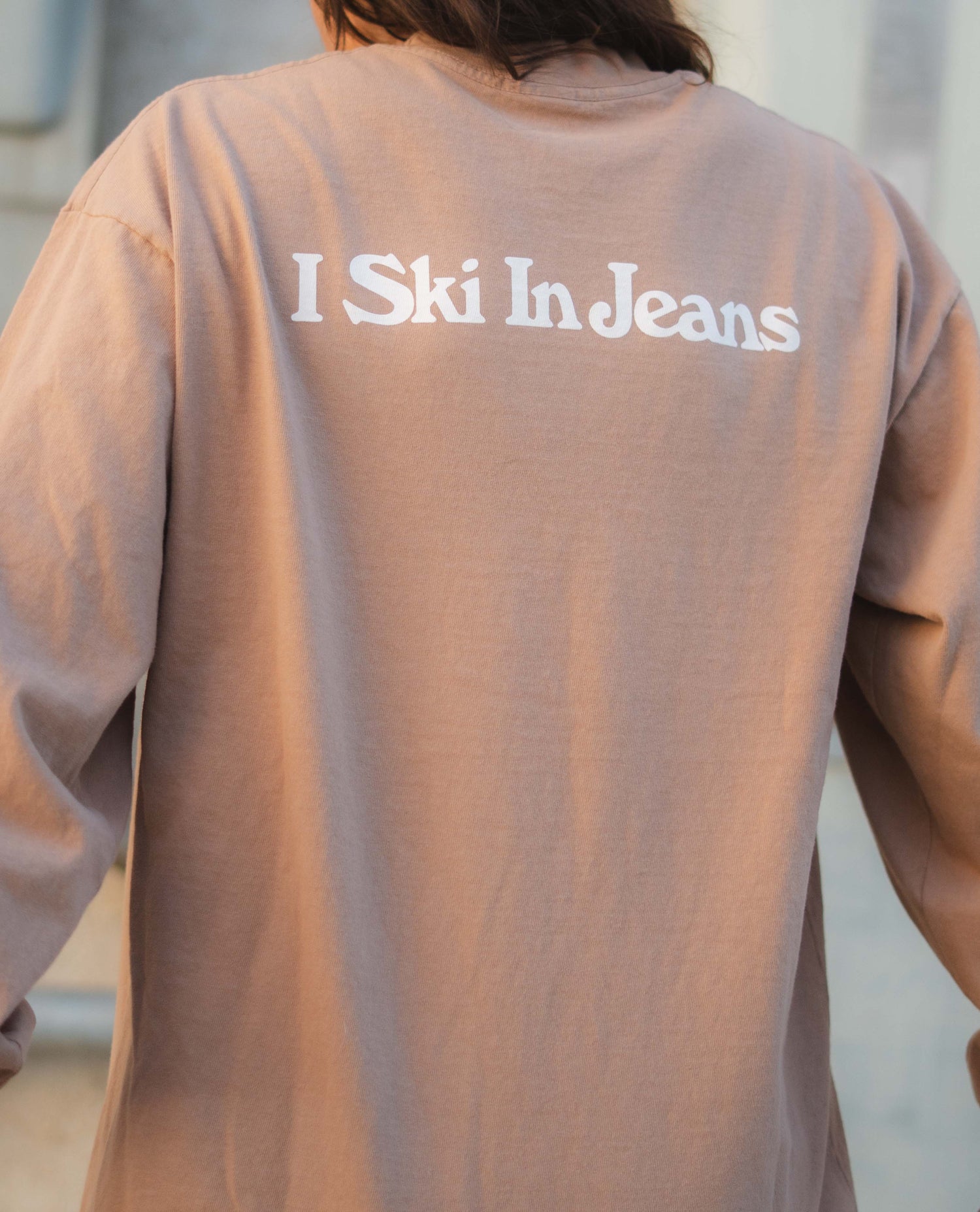 Person wearing a beige shirt with 'I Ski In Jeans' text on the back.