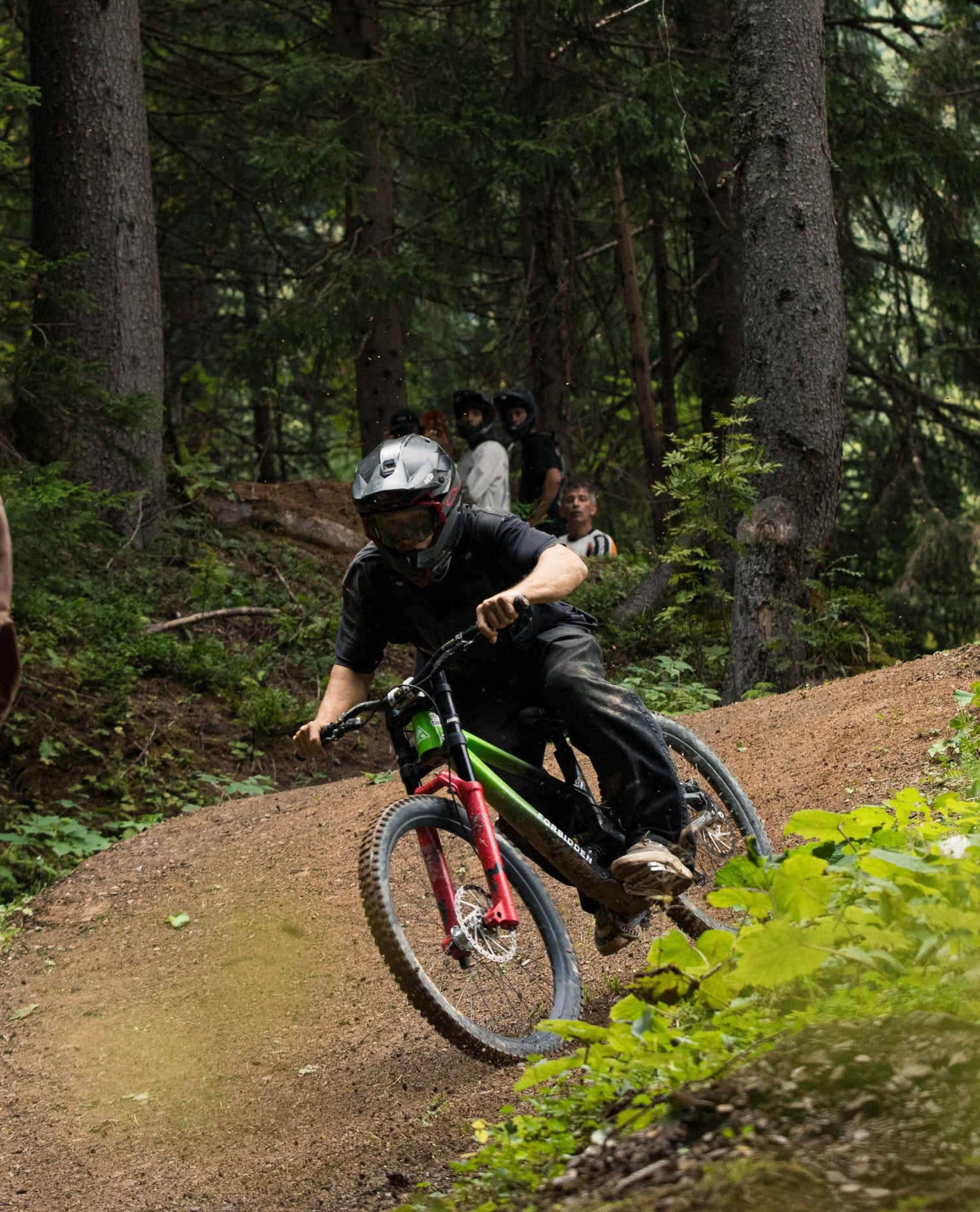 Person riding a mountain bike on a trail with trees and other riders in the background