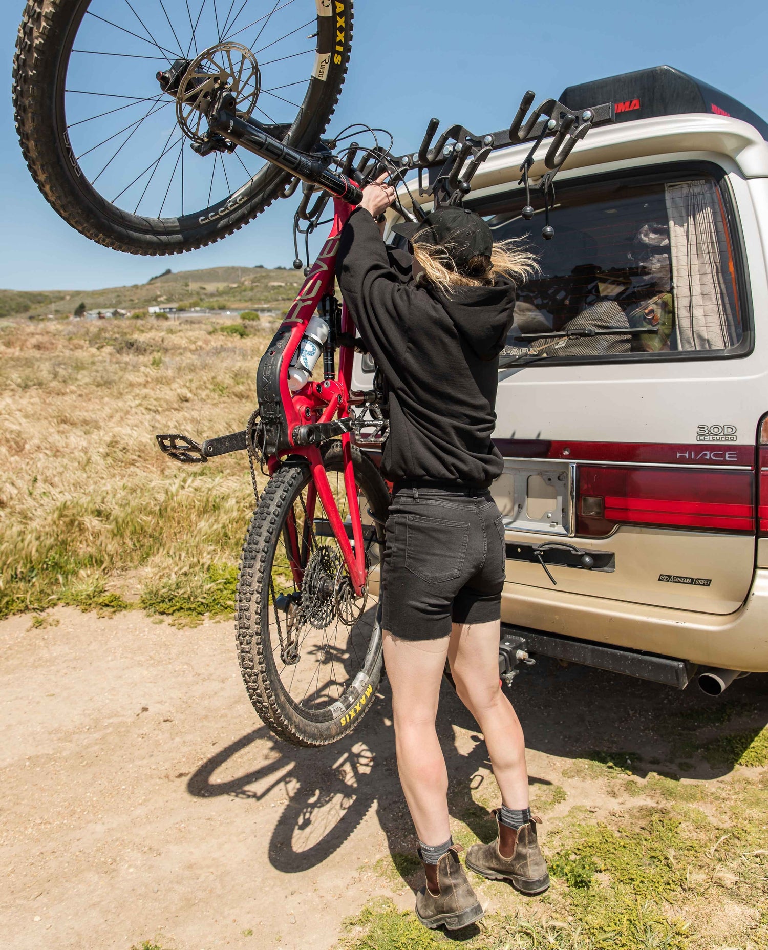 Person loading a bicycle onto a car with a bike rack in an outdoor setting.