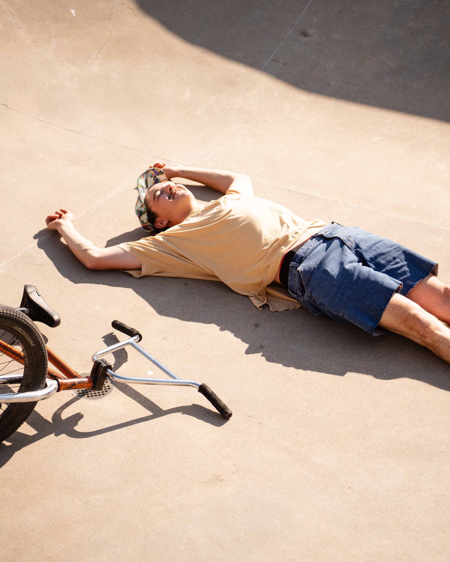 Man lies on the floor of a skatepark bowl after crashing his bmx bike. He is wearing Ripton DTJ shorts. 