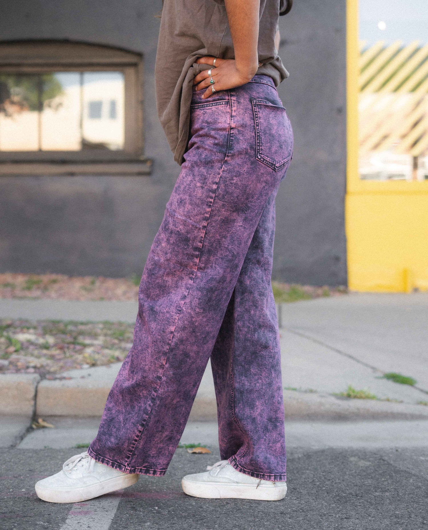 Person wearing purple acid-wash jeans and white sneakers on a street.