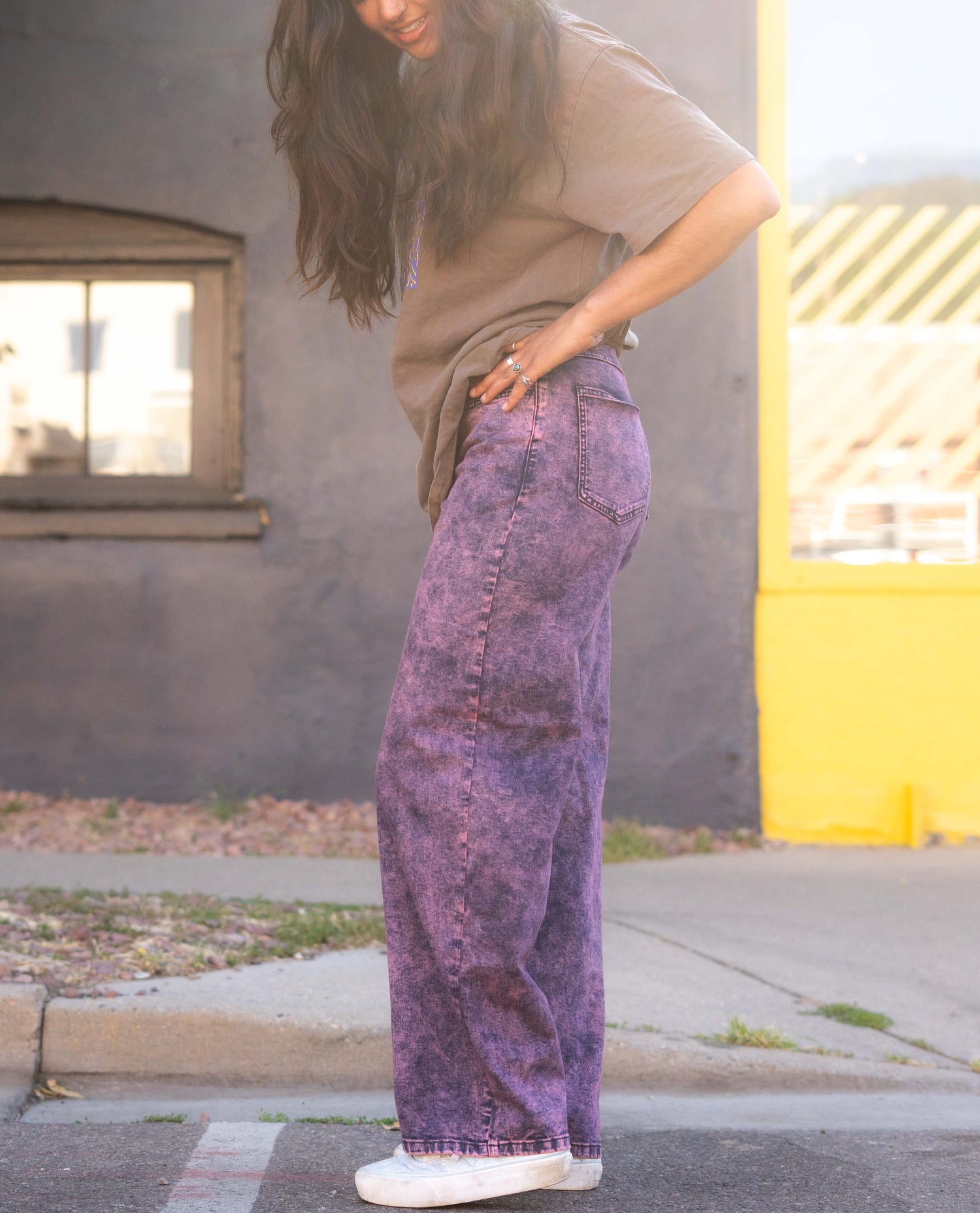 Person wearing a beige shirt and purple patterned pants standing on a street.