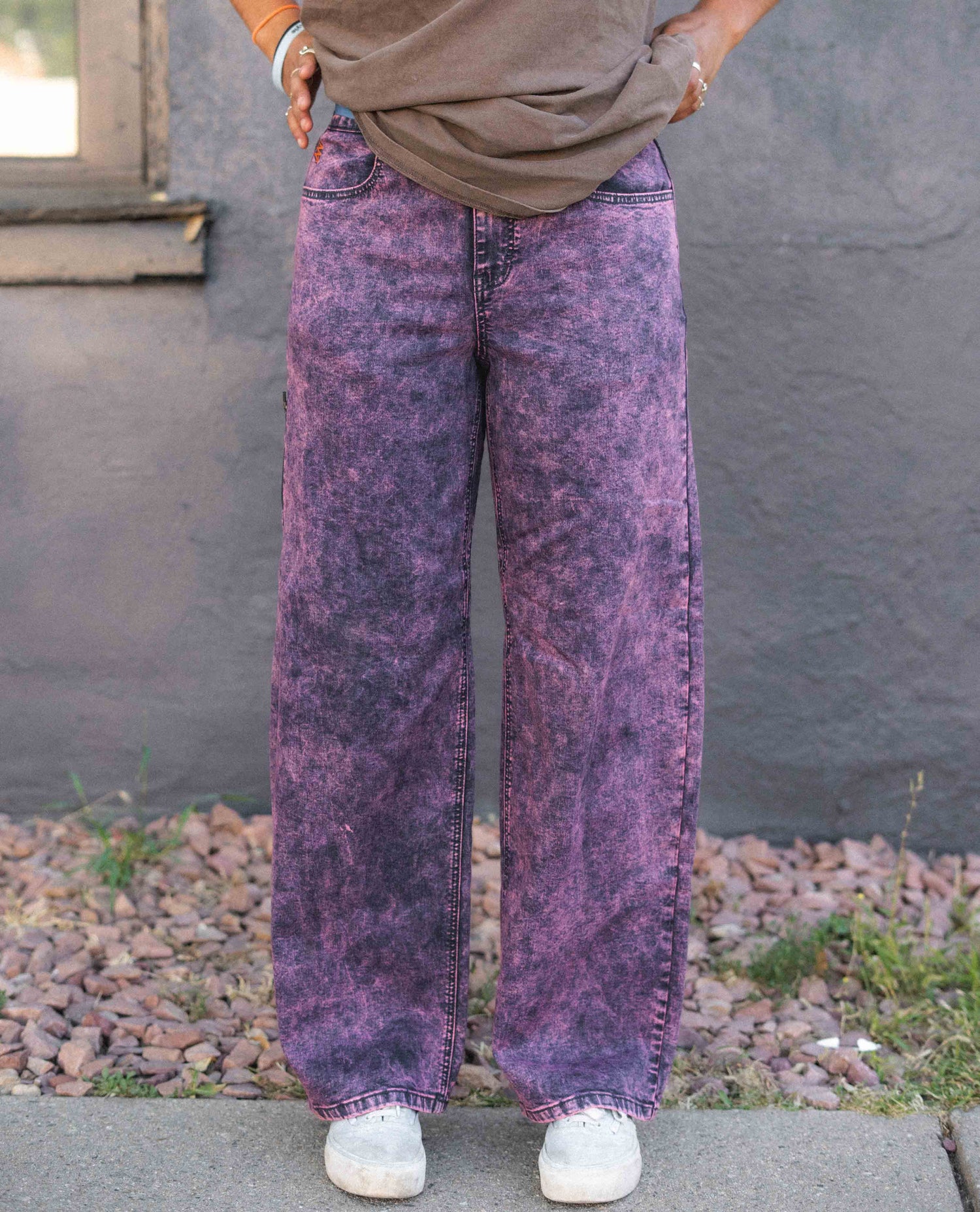 Person wearing purple acid-wash jeans standing against a gray wall.