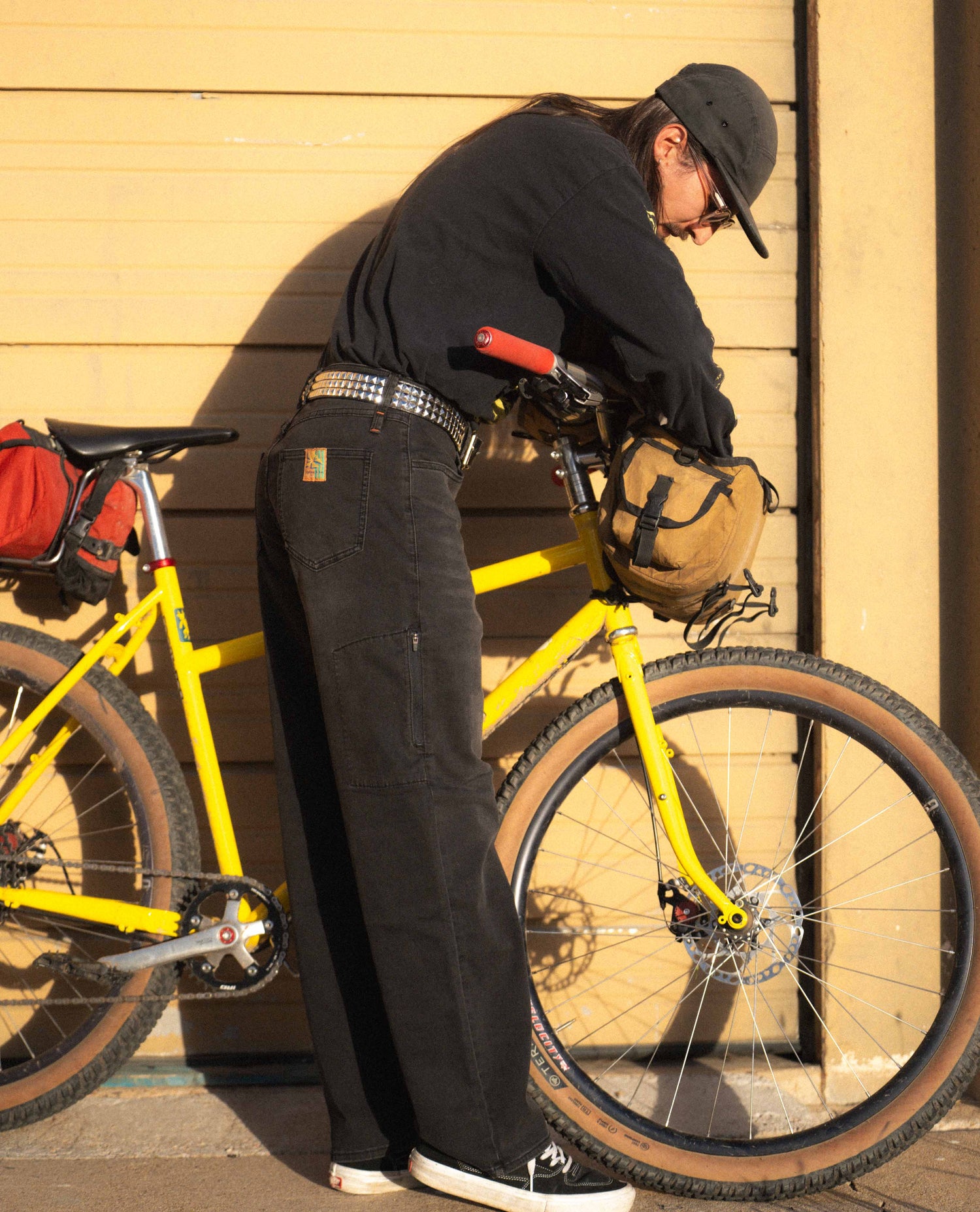Person adjusting a yellow bicycle against a beige wall.
