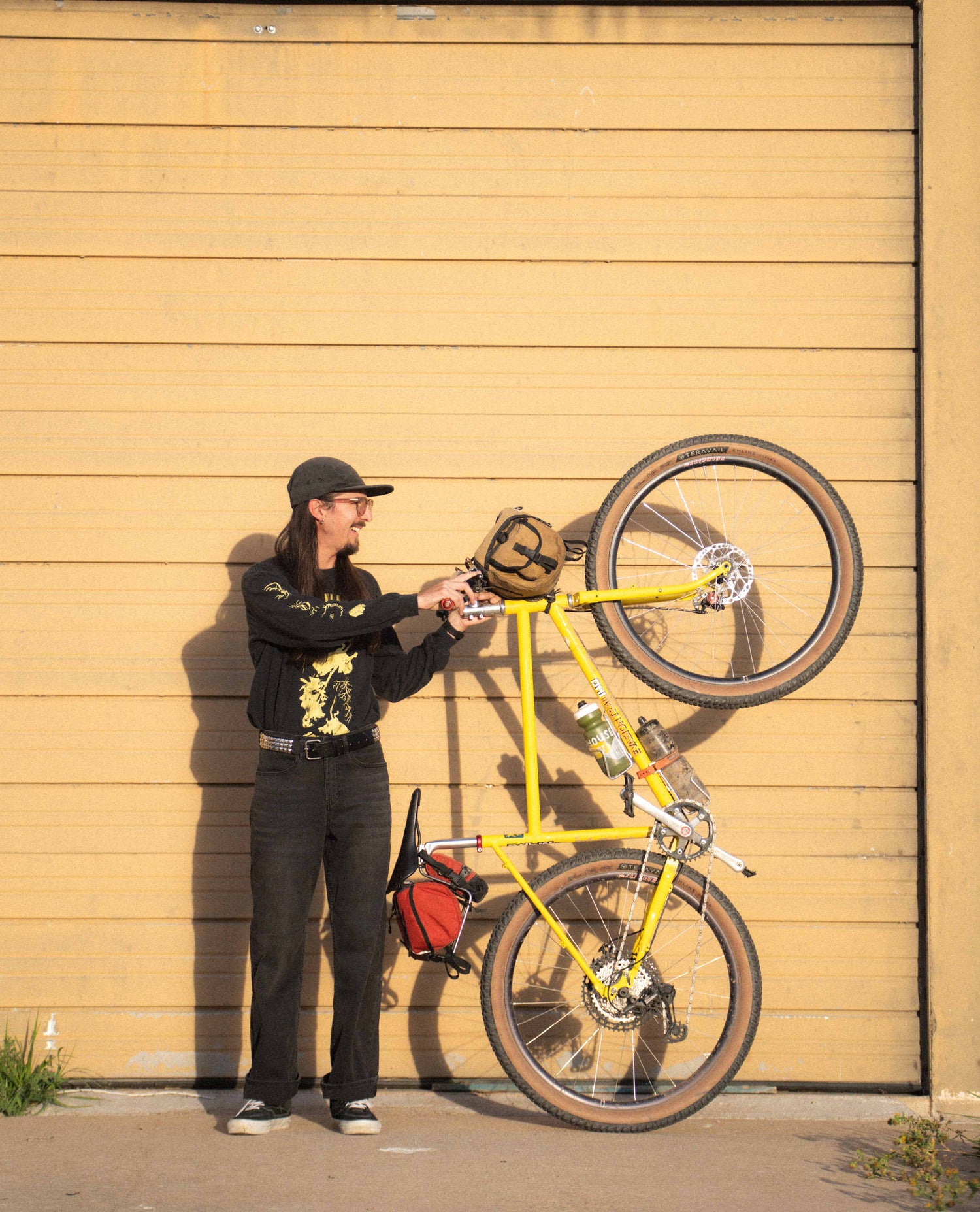 Person holding a yellow bicycle against a wooden wall