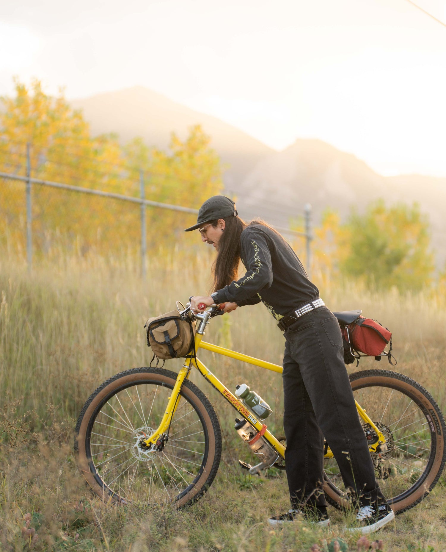 Person with a yellow bicycle in a field with mountains in the background