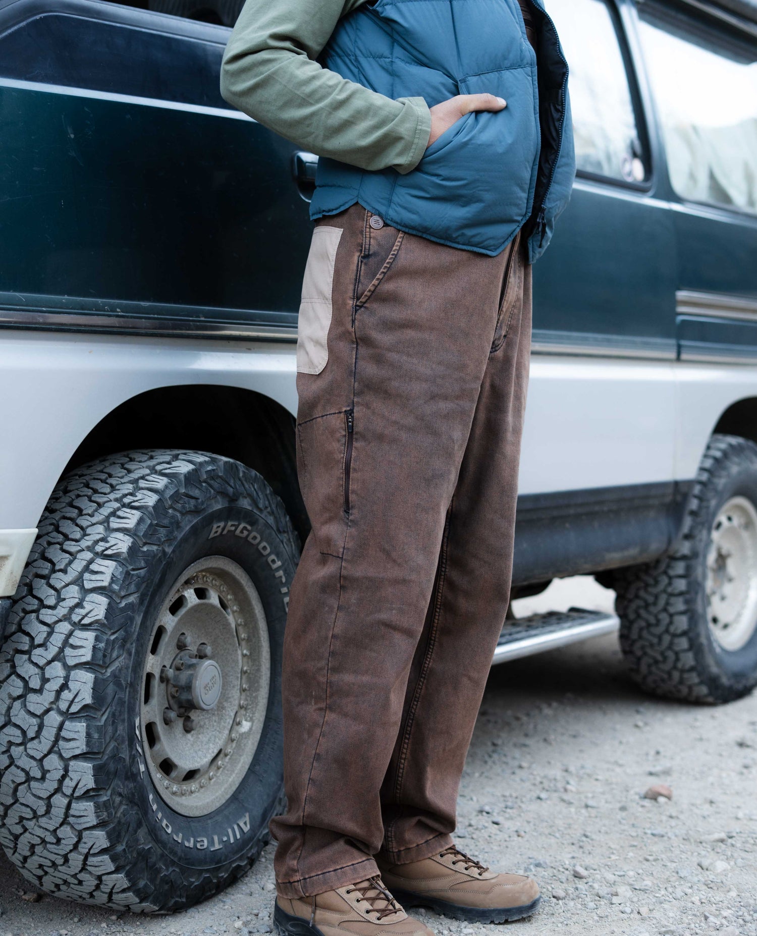 Person wearing brown pants and a blue jacket standing next to a vehicle.
