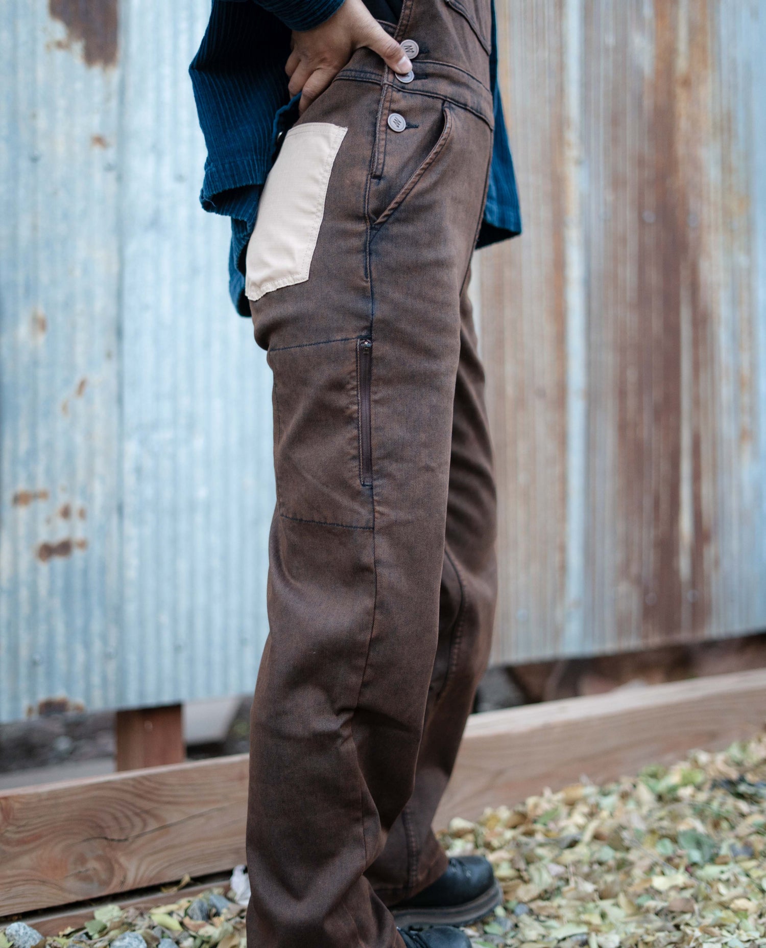 Person wearing brown work pants with a white patch in front of a corrugated metal wall.