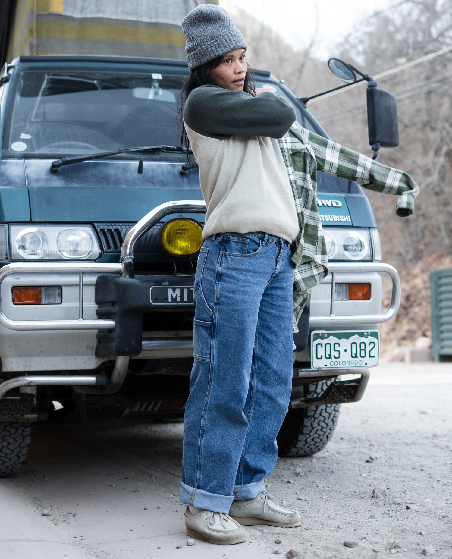 Person standing next to a vehicle with a plaid shirt and jeans