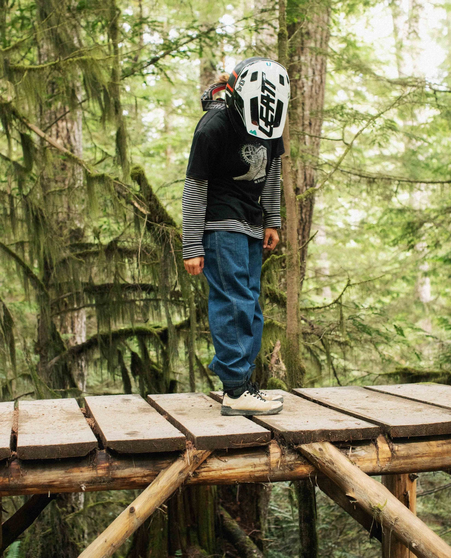 Person wearing a helmet and black jacket standing on a wooden bridge in a forest