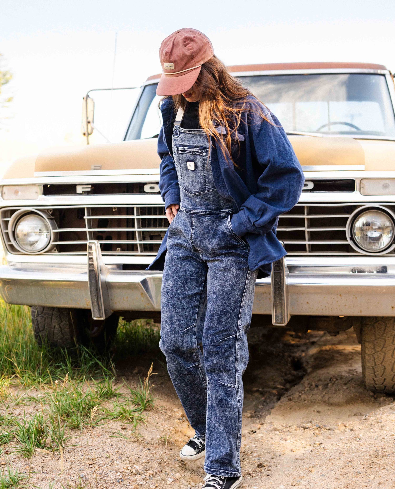 Woman wearing Indigo Marble denim overalls in front of a truck