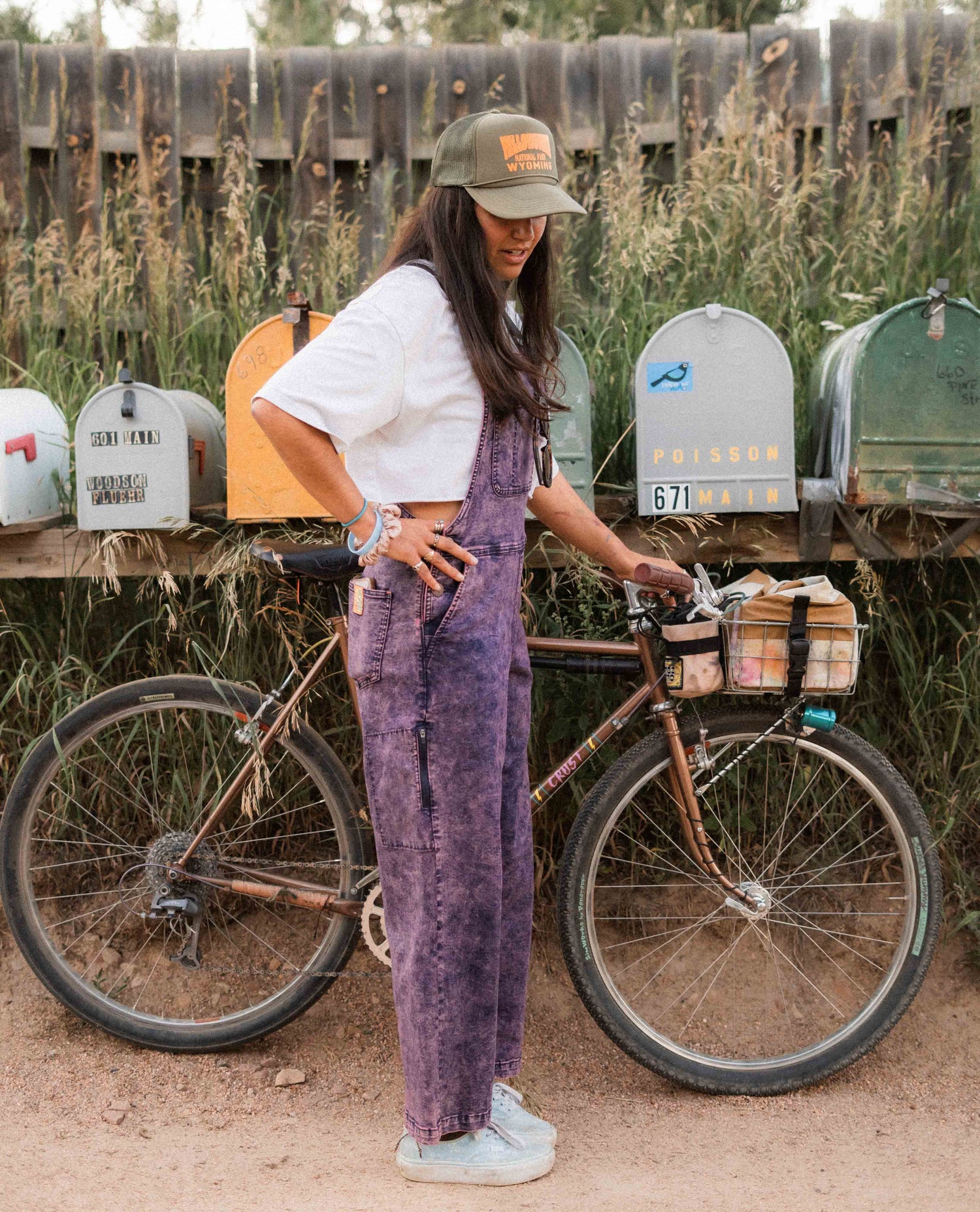 Person in purple overalls standing next to a bicycle with mailboxes in the background
