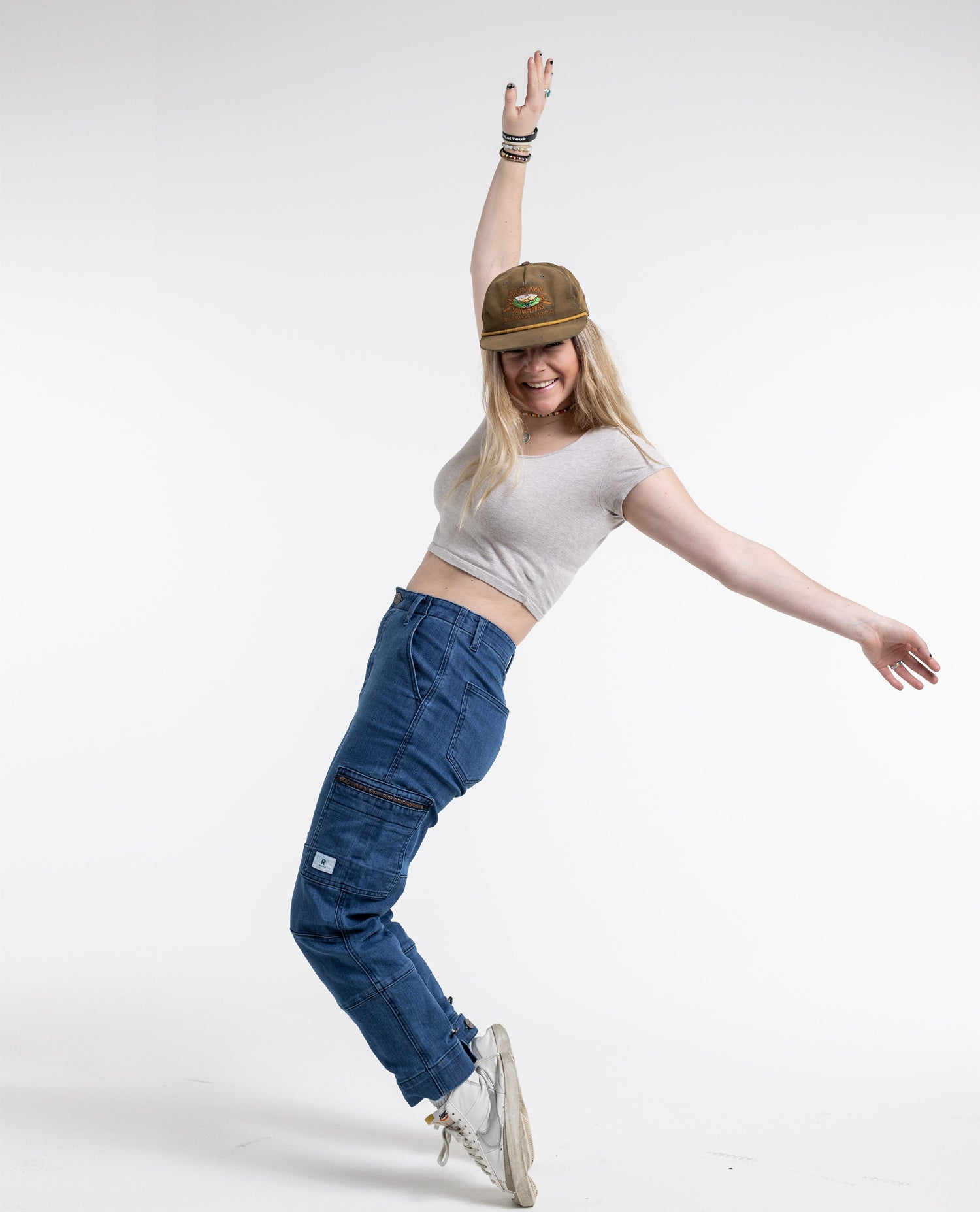 A model posing playfully in a grey crop top and blue ripton pants. 