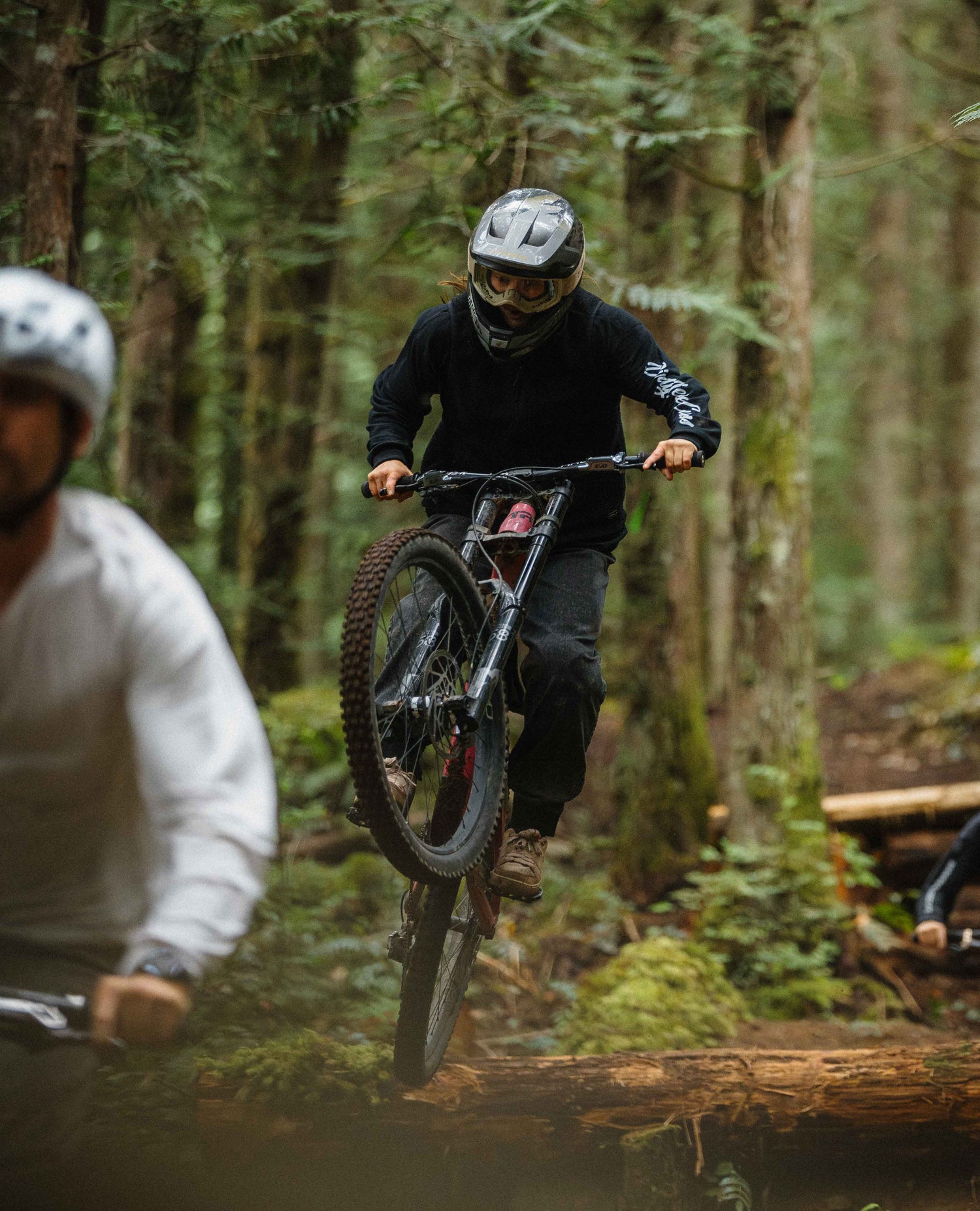 Two mountain bikers navigating a log in a forest setting