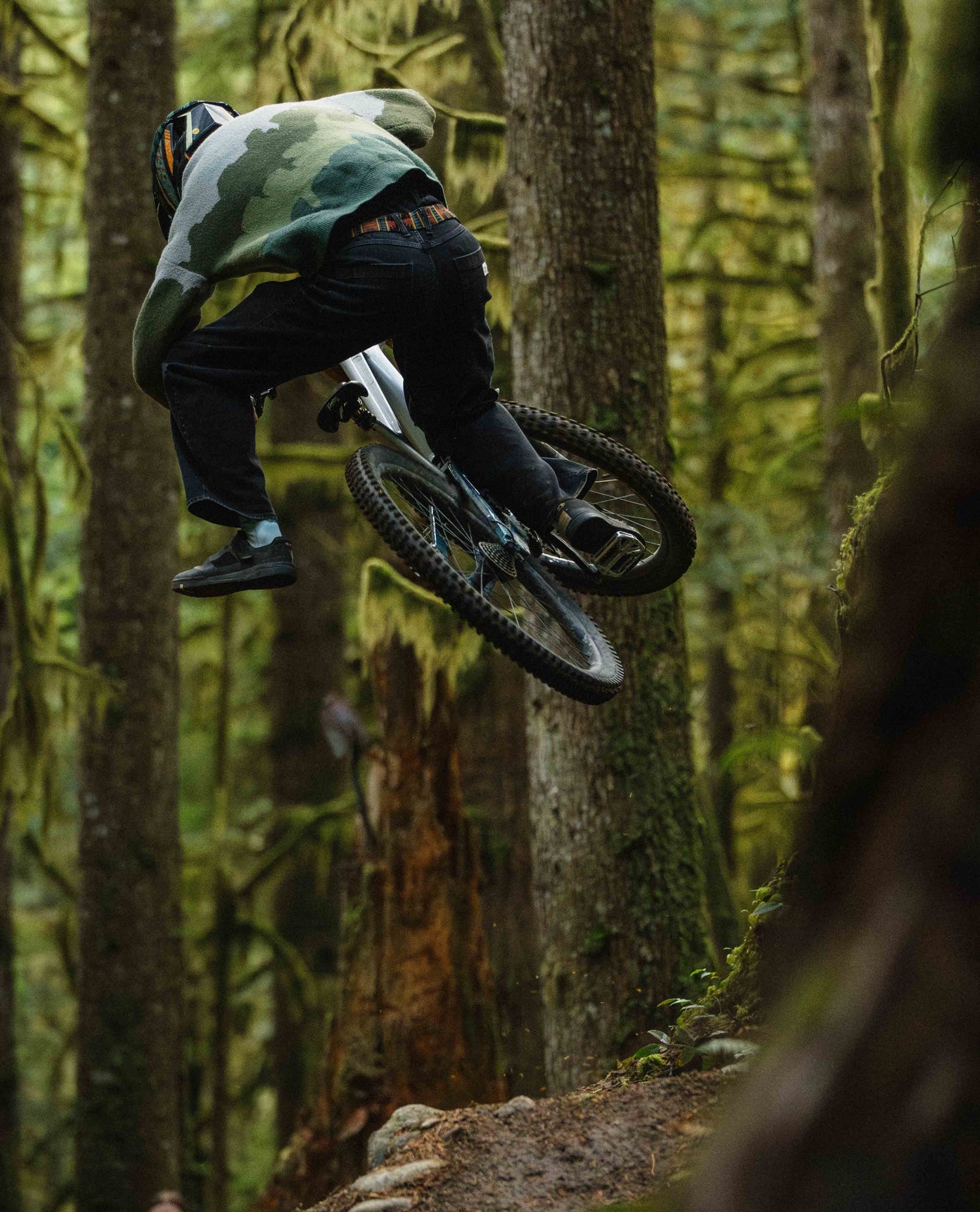 Person on a mountain bike in mid-air over a log in a forest