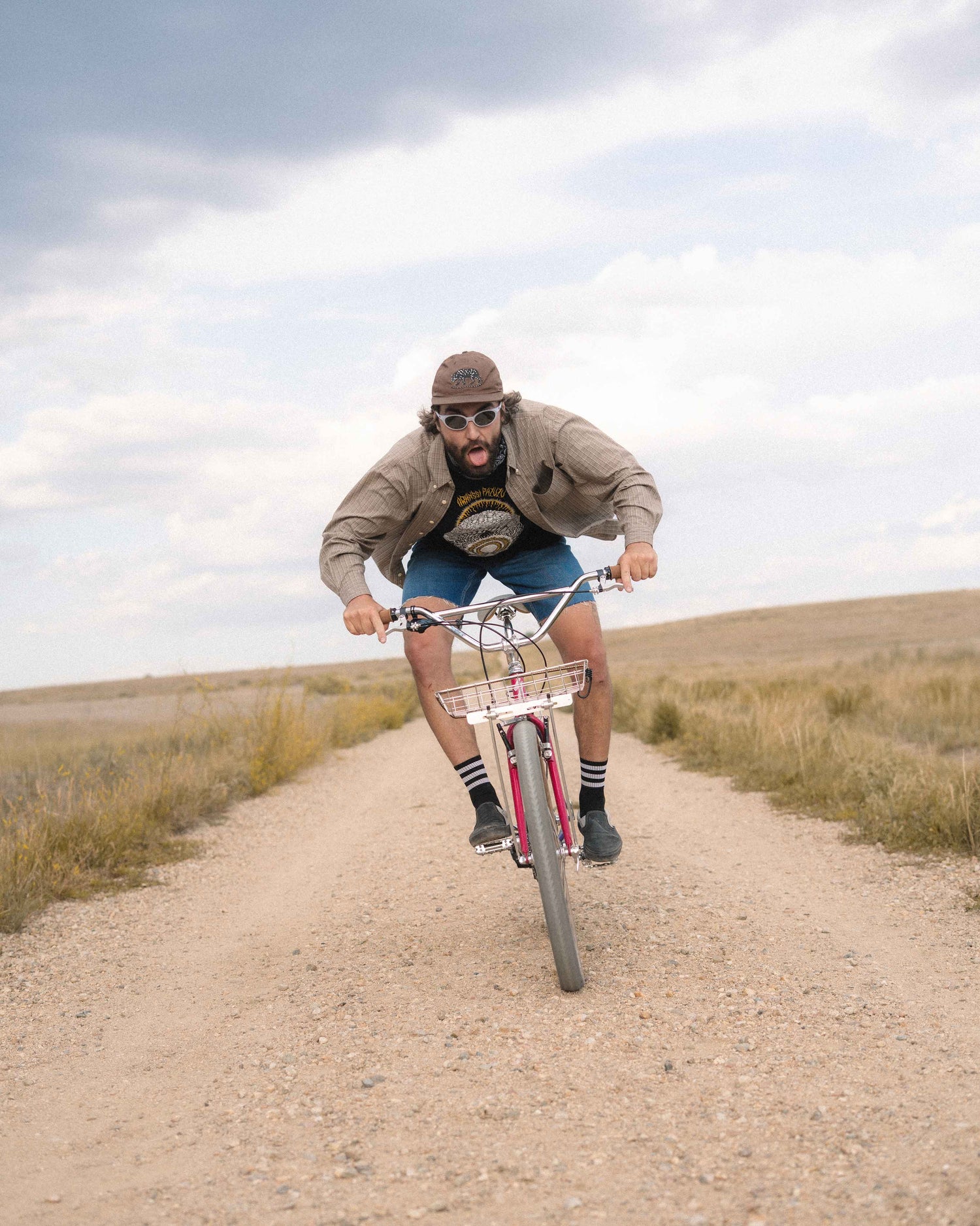 A man riding a red and white mountain bike on a dirt path in an open grassy landscape under a cloudy sky.