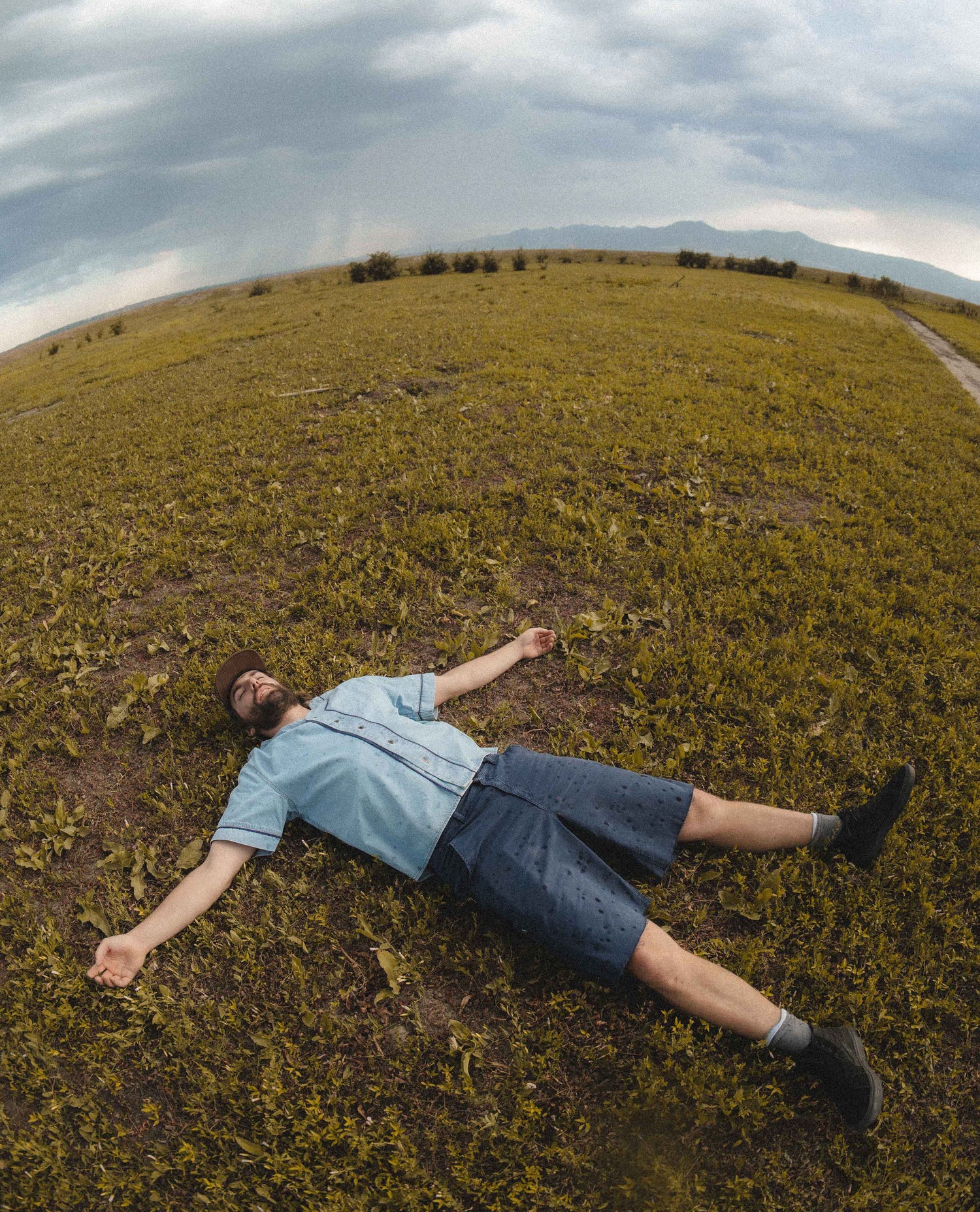 A man wearing denim laying in a grass field on a cloudy day. 