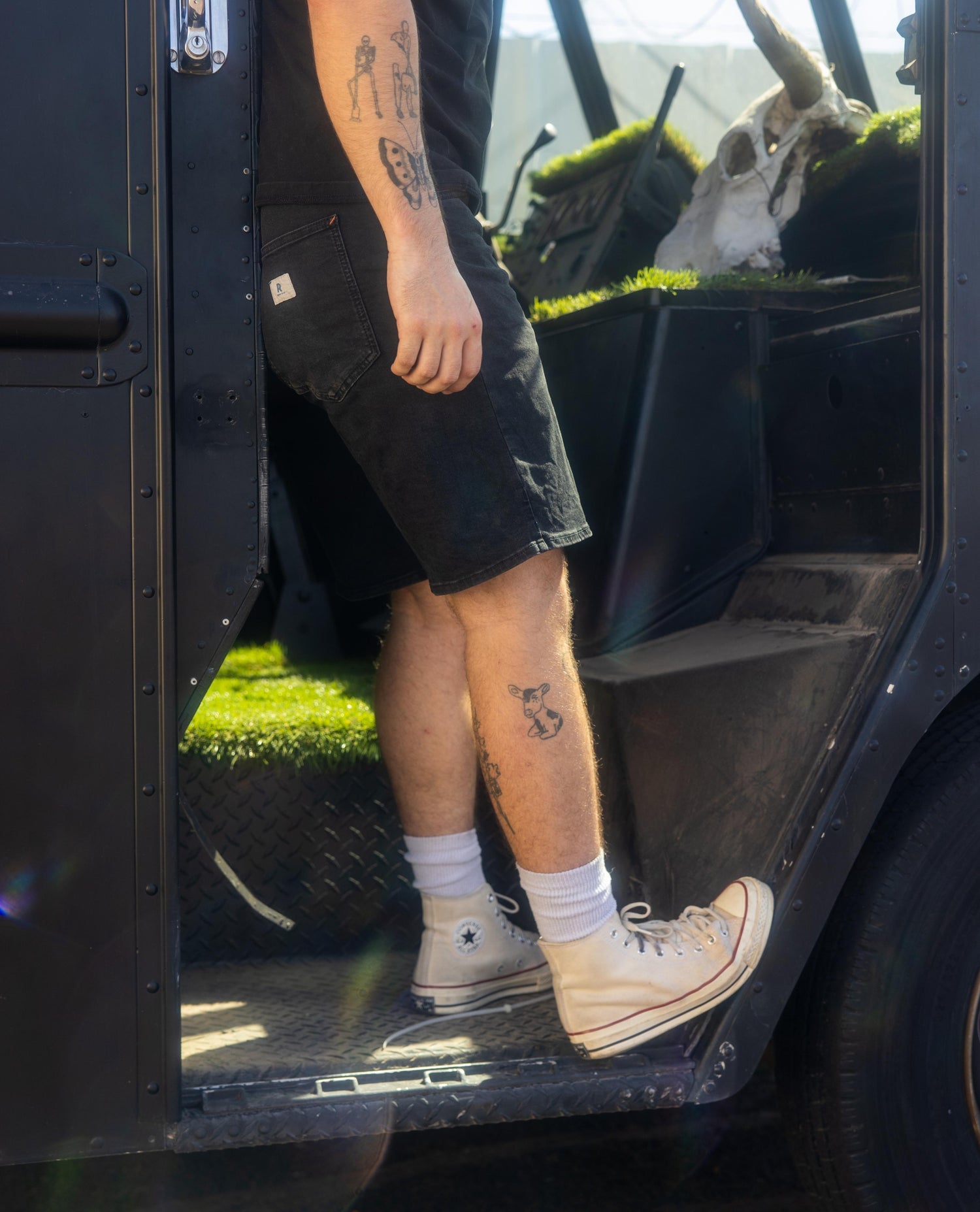 Person wearing black shorts and beige Converse shoes stepping out of a vehicle with grass visible outside.
