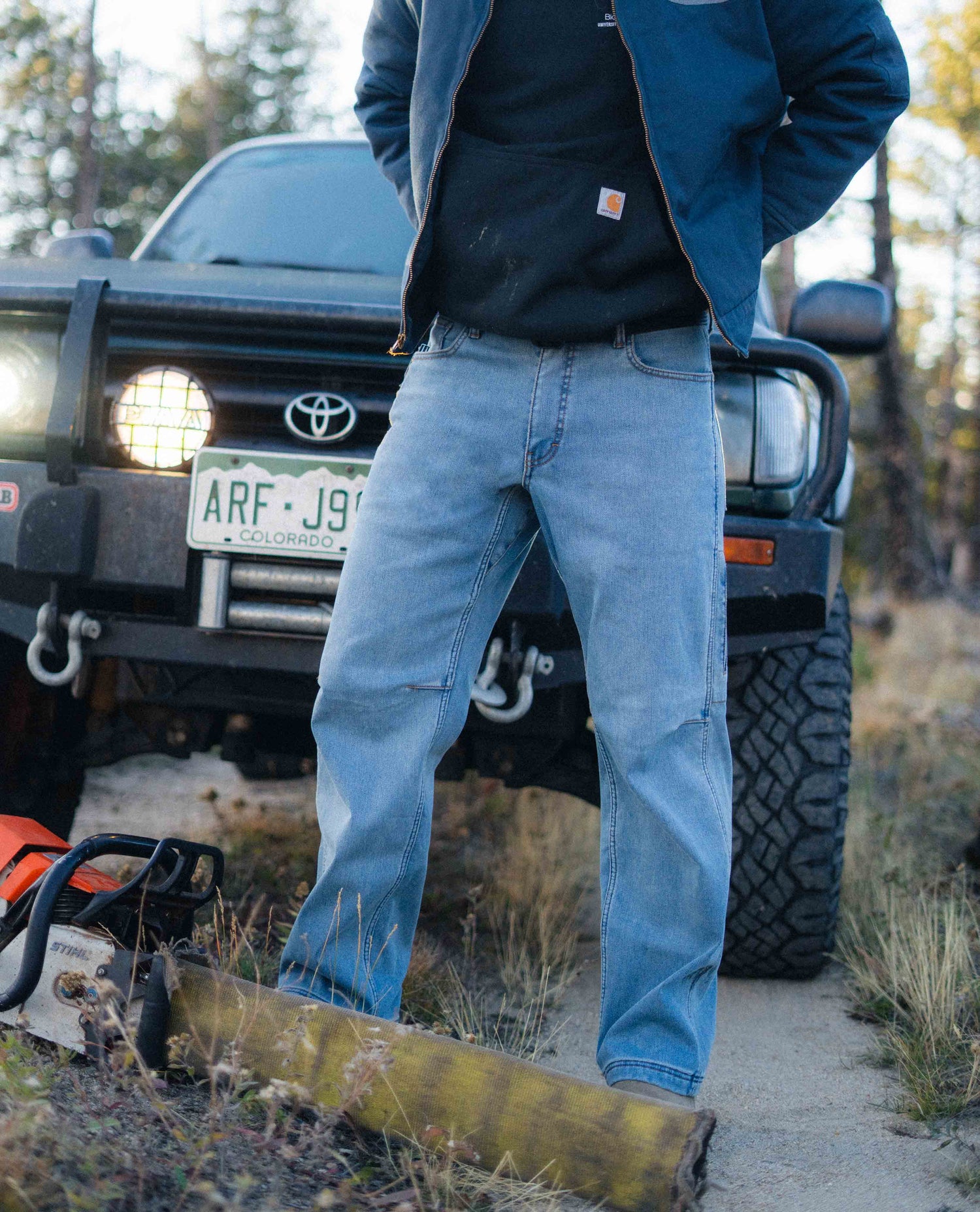 Person wearing blue jeans standing in front of a Toyota truck in a natural setting
