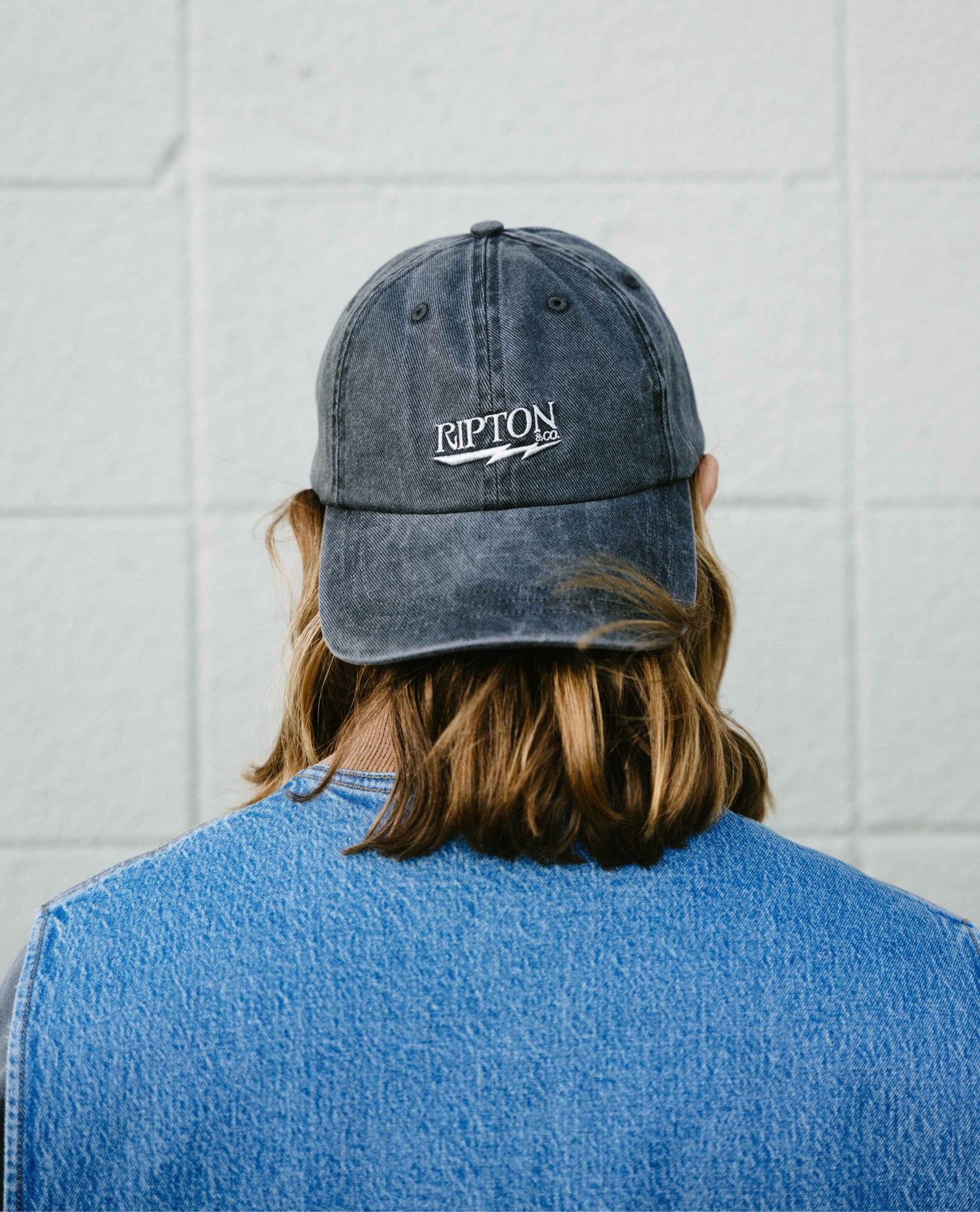 Person wearing a blue denim cap with 'Ripton' logo against a white tiled wall