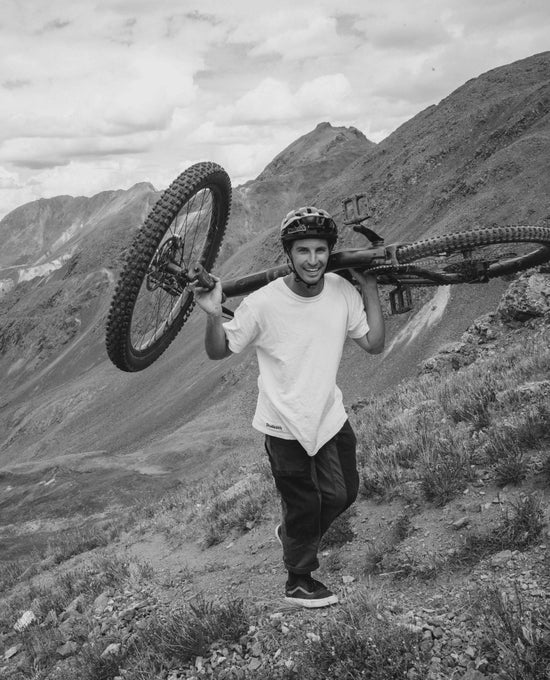 Jon carrying a mountain bike on a mountainous landscape