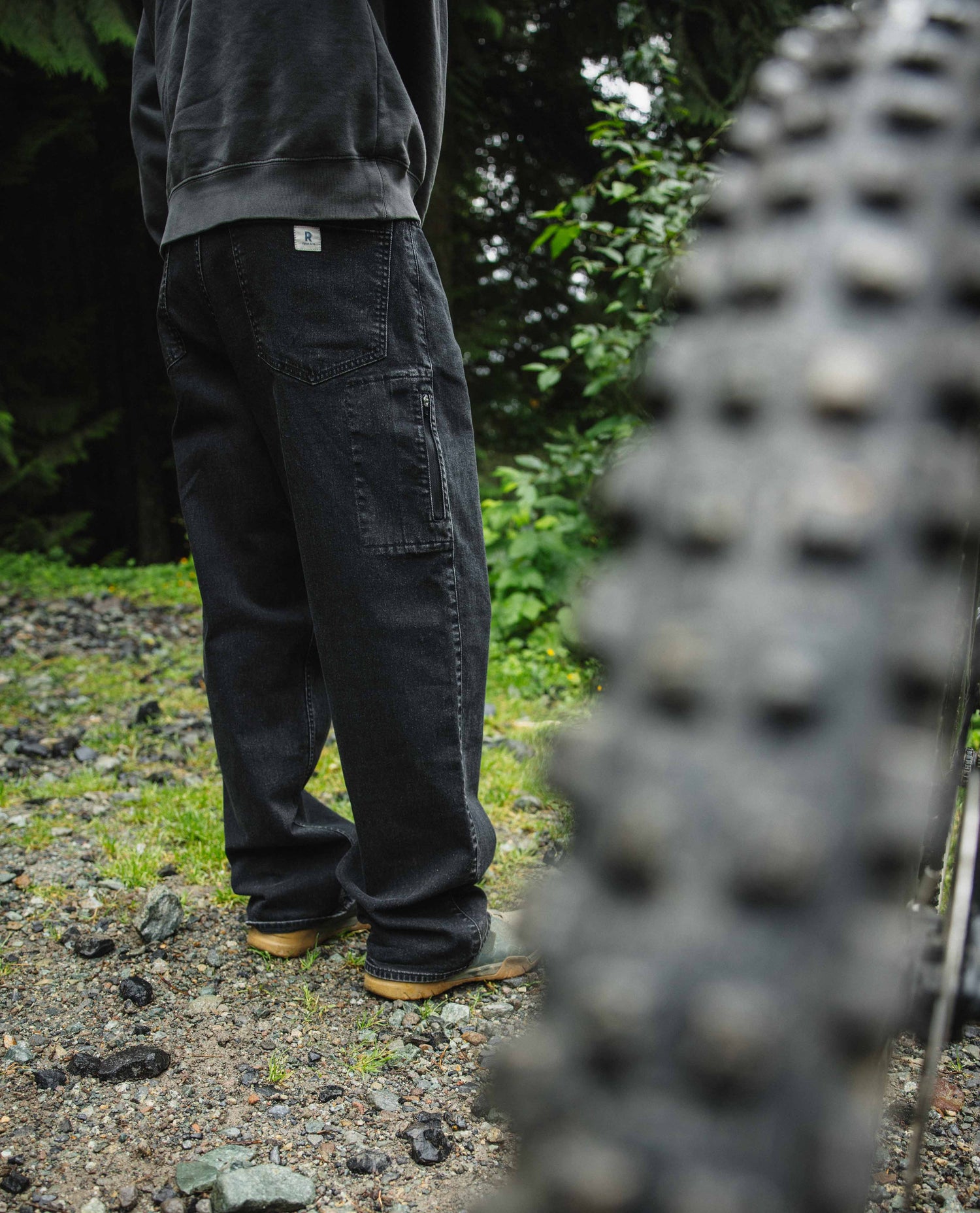 Person wearing dark pants standing outdoors with a close-up of bike tires in the foreground.