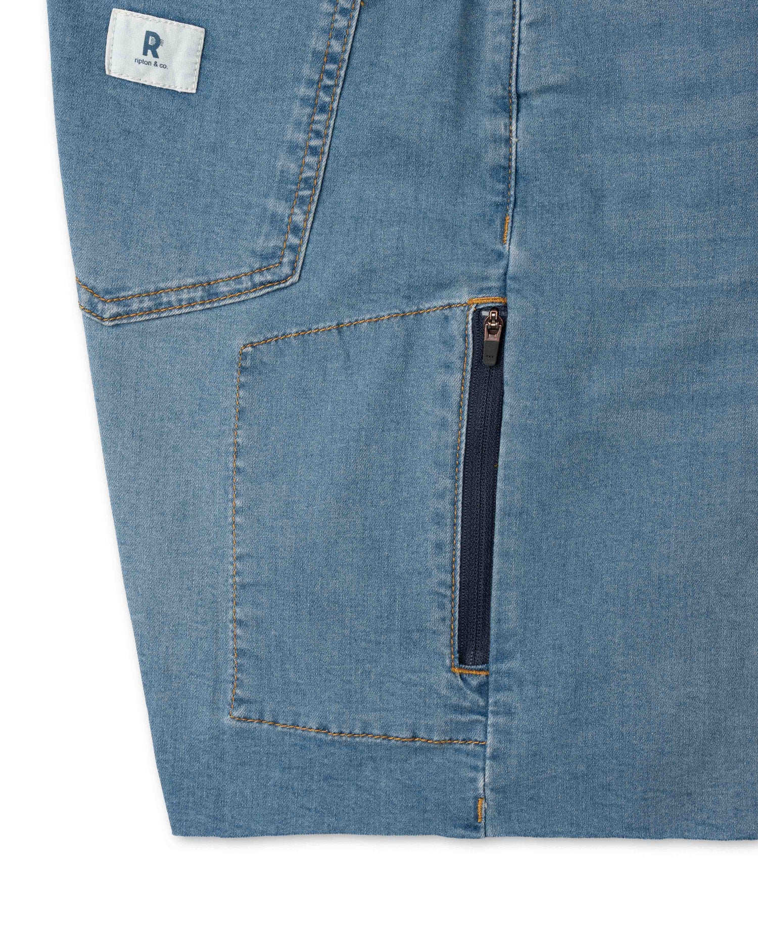 Close-up of blue denim shorts with a zipper pocket and brand label.