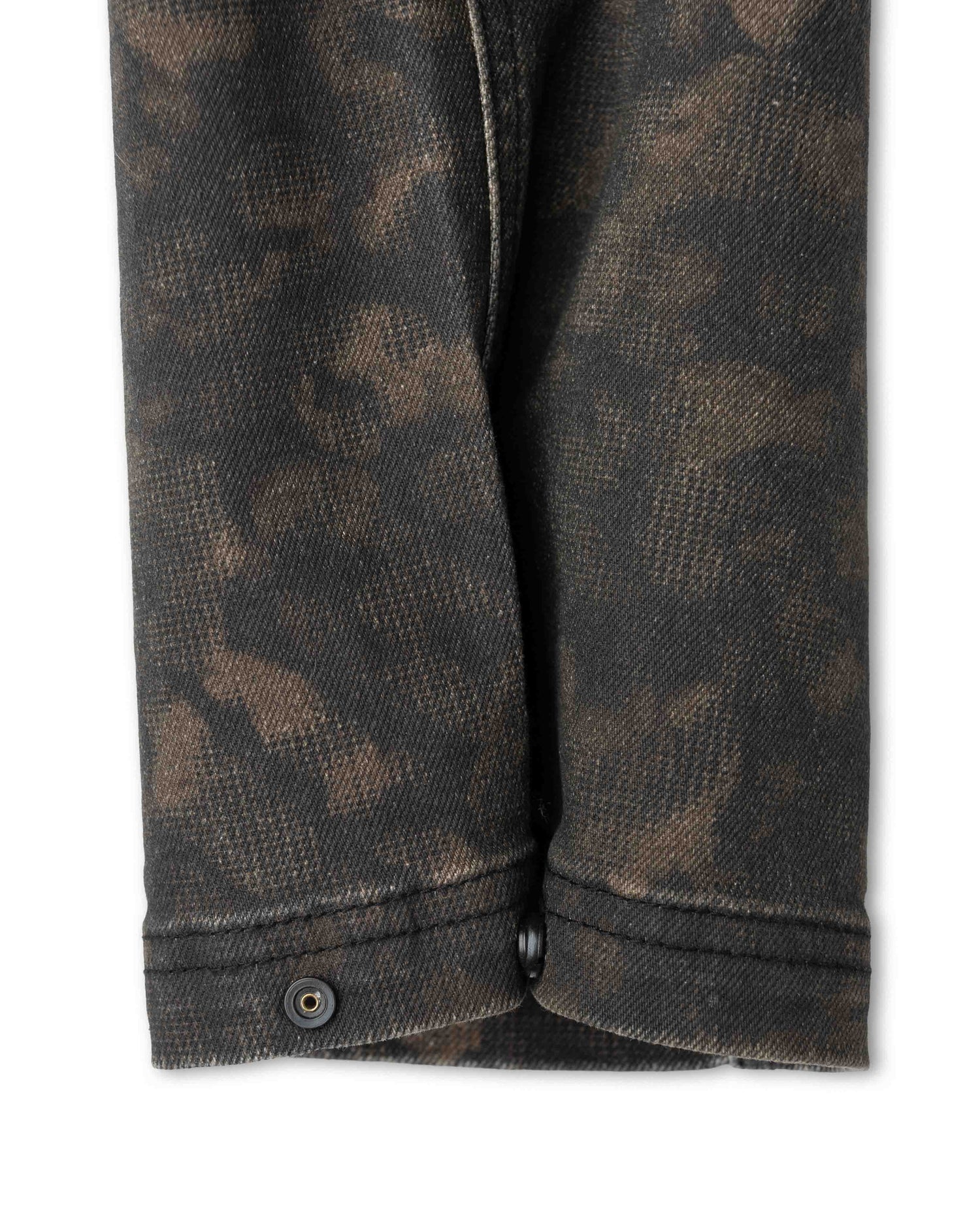 Close-up of a dark brown and black camouflage patterned denim fabric, showing the texture and a buttoned cuff.