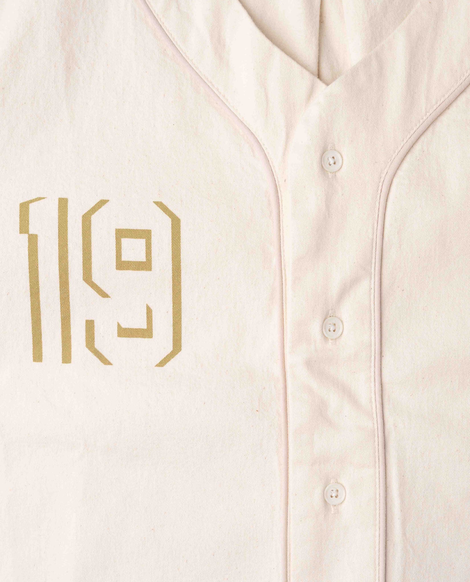Close up photo of white shirt with gold 19 detail