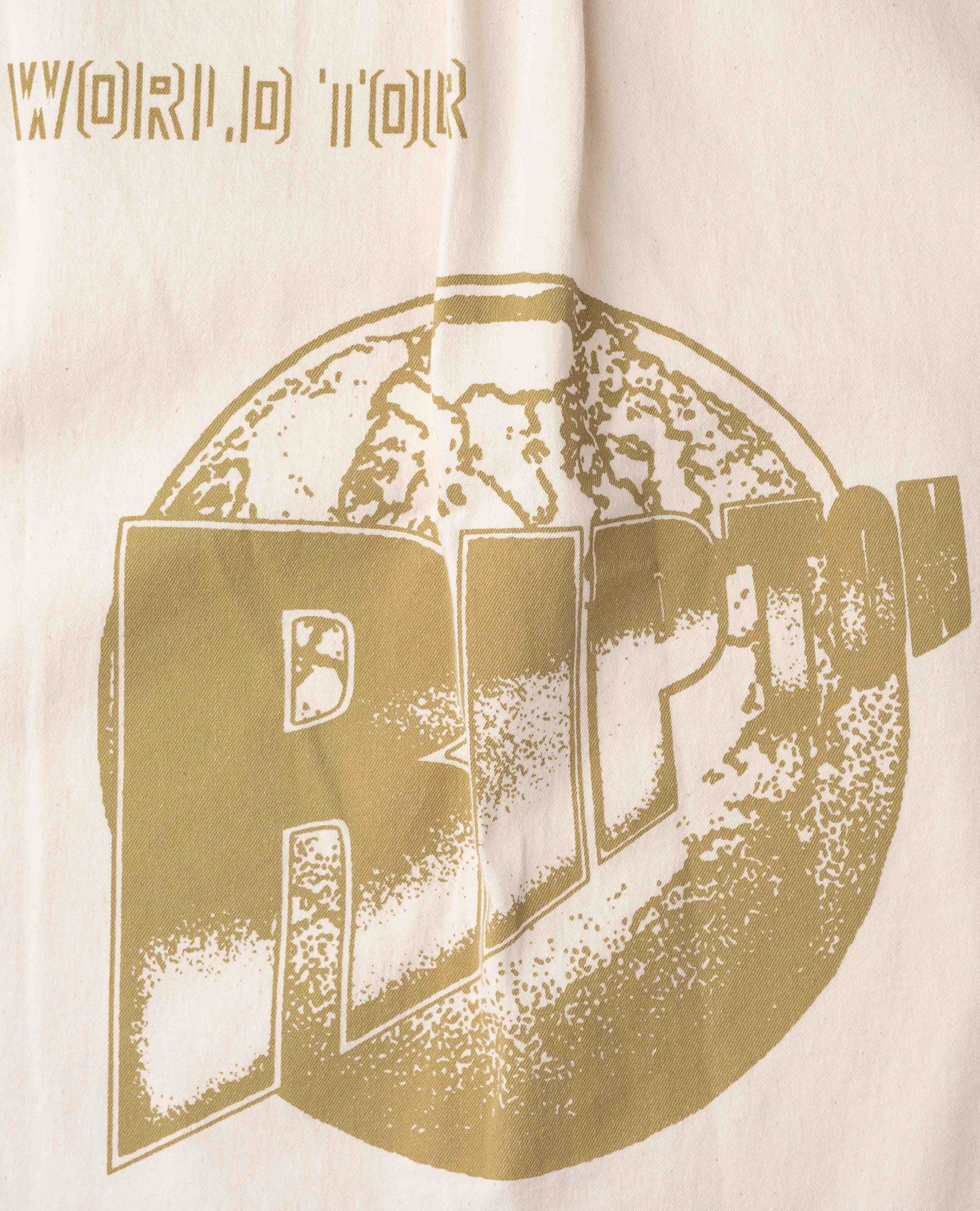 Close up of gold Ripton logo on white shirt.