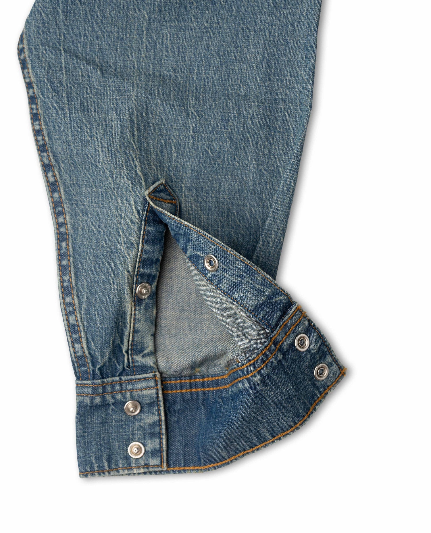 Close-up of a blue denim garment, showing the fabric texture, stitching, and metal snap buttons on a white background.