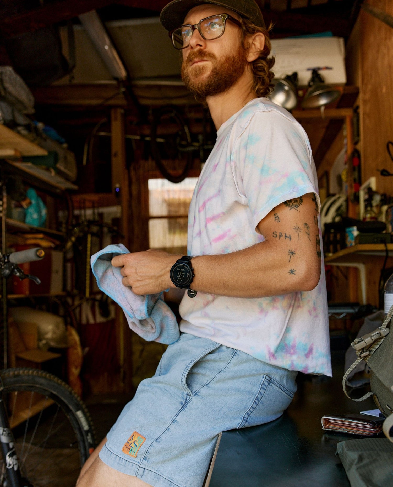 Man in a workshop holding a cloth, wearing a colorful shirt and jeans.