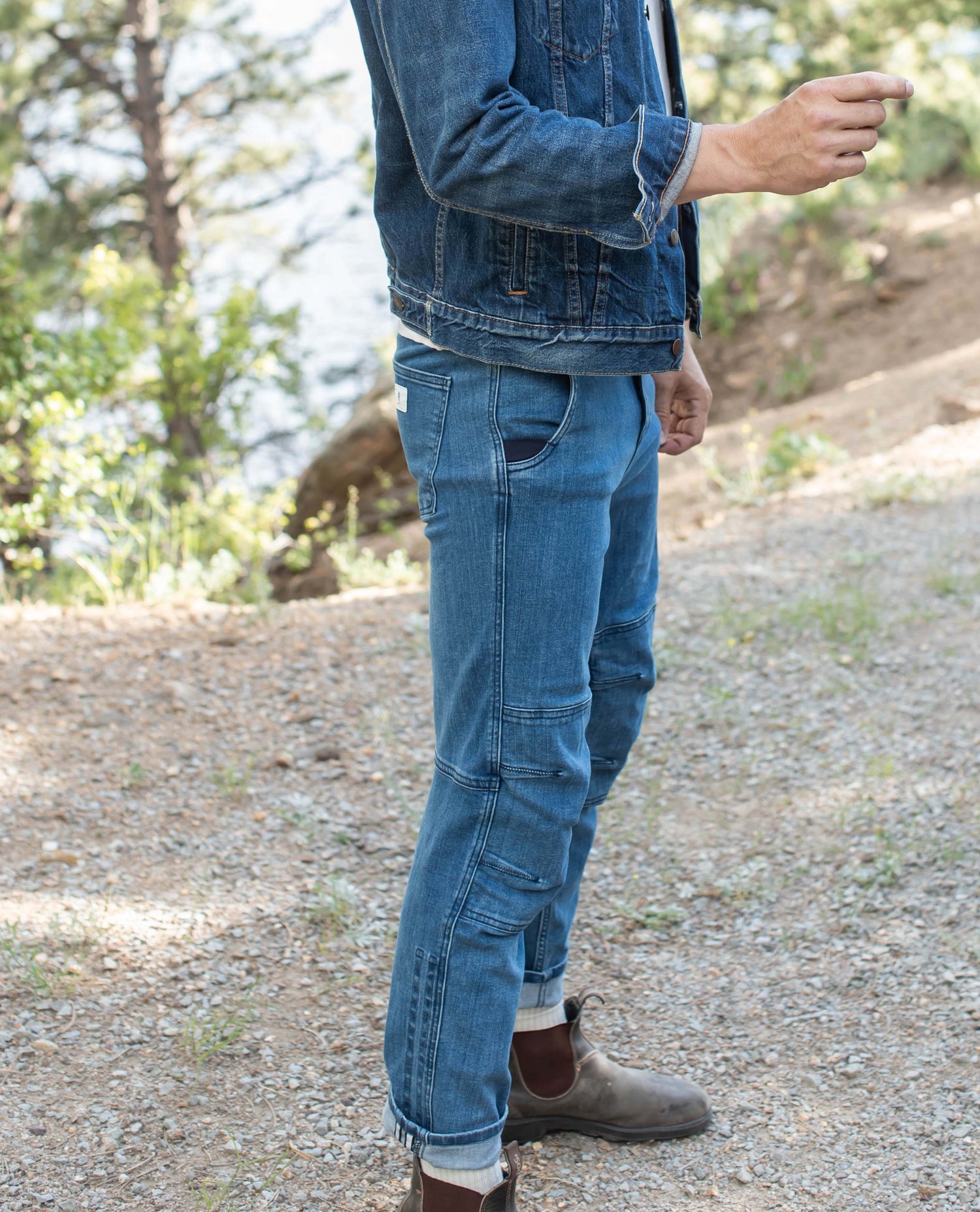 Profile view of a man wearing a pair of blue jeans and a denim jacket with brown shoes.