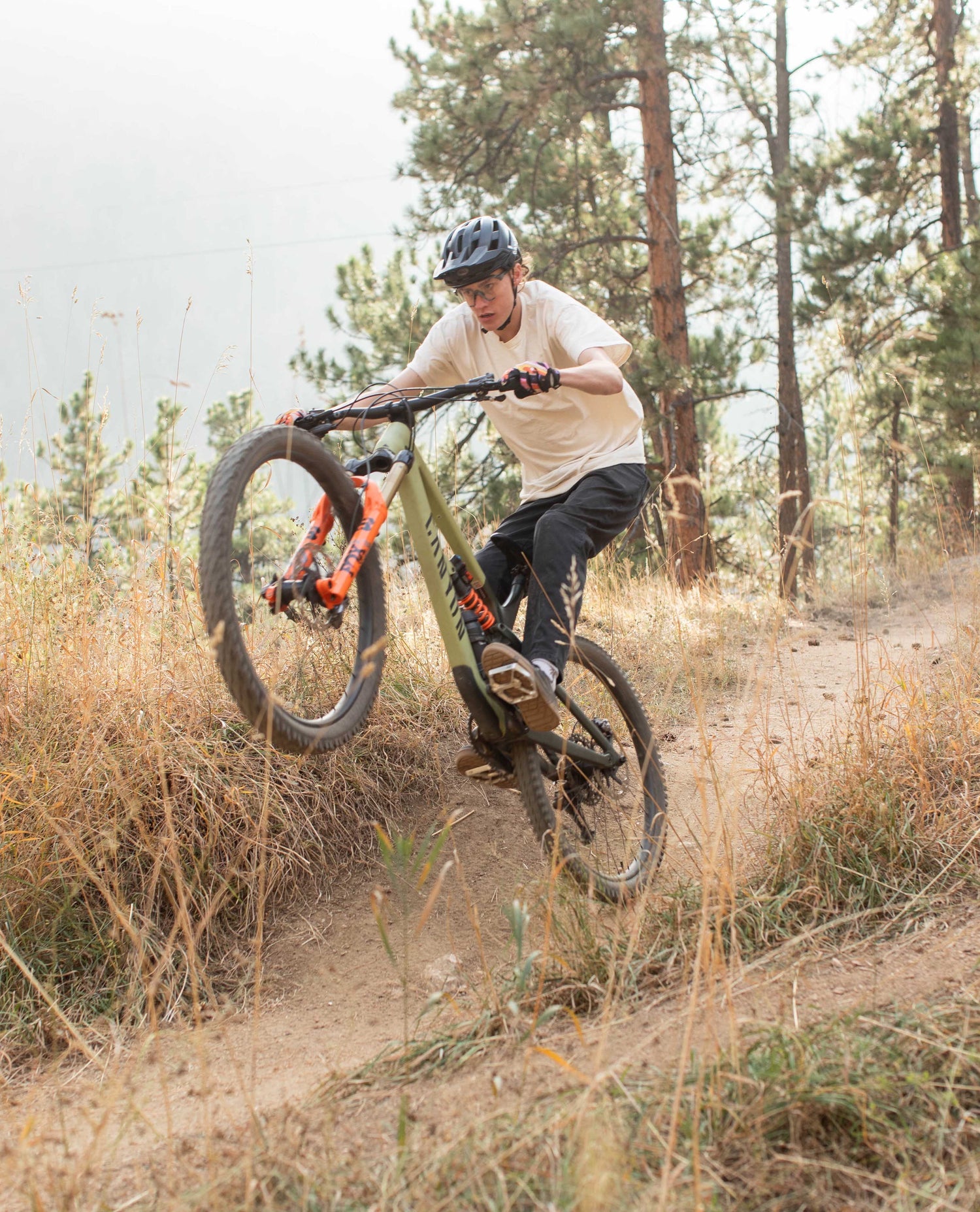 A man doing a wheelie on his mountain bike. he is wearing a helmet, white t shirt and black pants. 