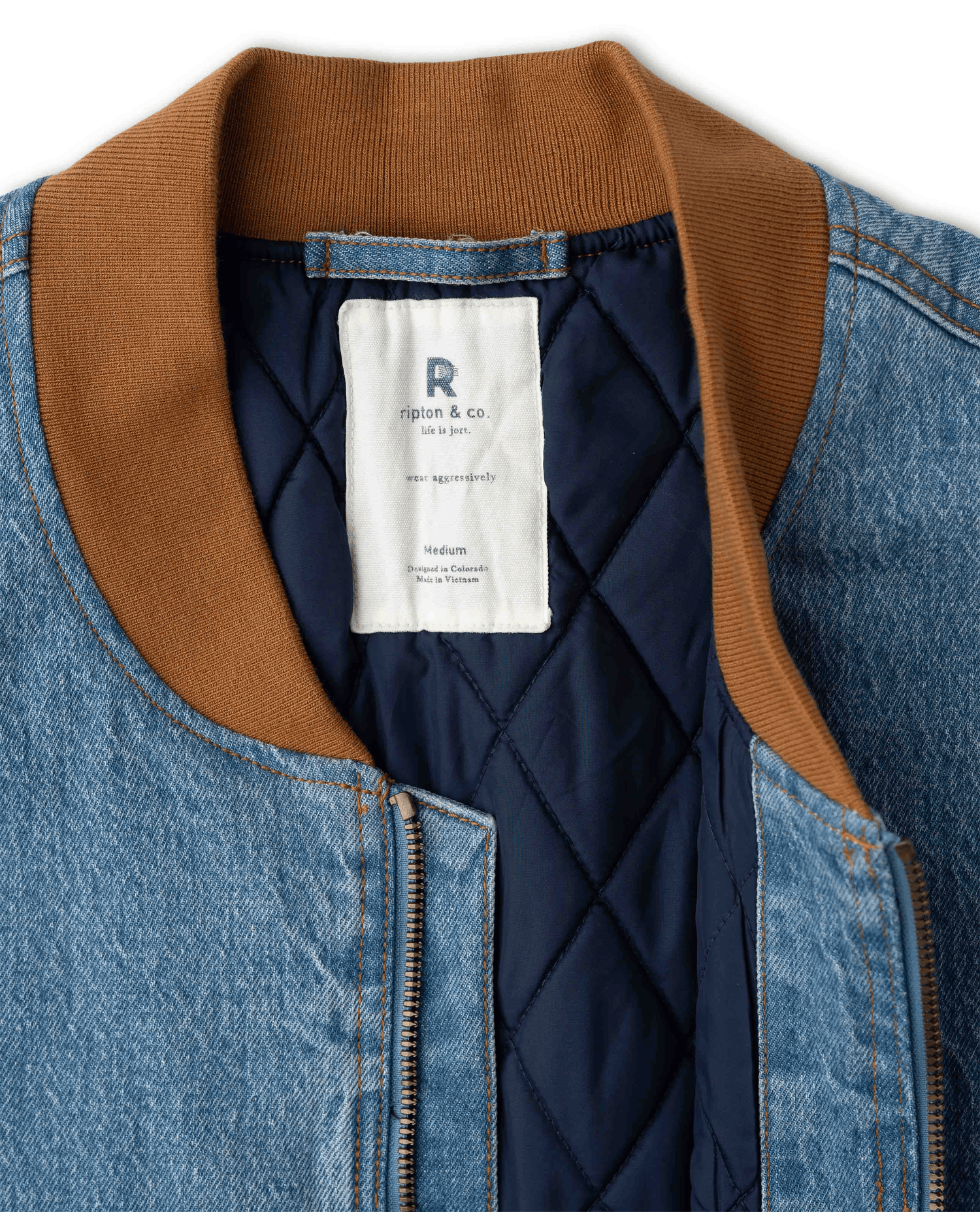 Close-up of a denim jacket with a brown ribbed collar, a dark navy quilted lining, and a white interior brand label reading Rigion & Co.