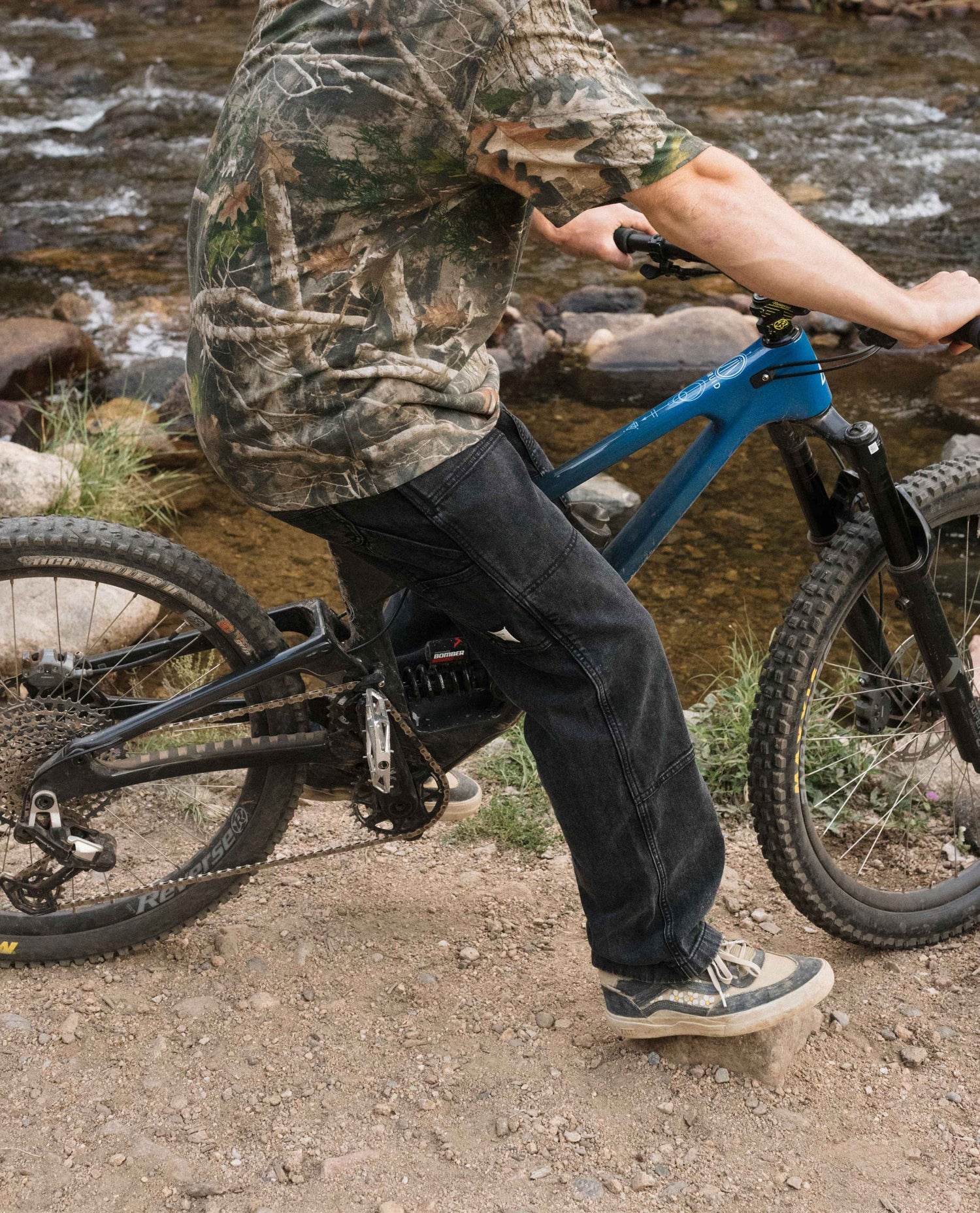 Person riding a blue bicycle on a rocky trail near a stream