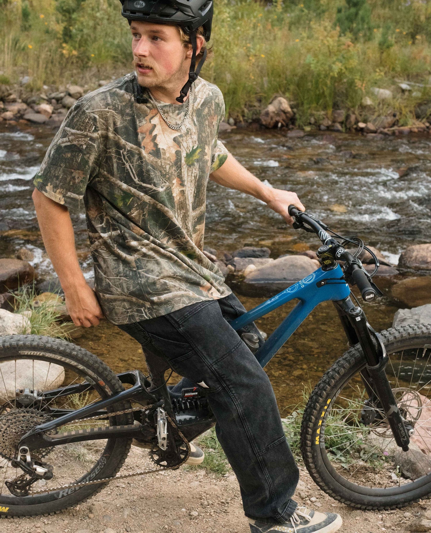 Person with a bicycle near a stream in a natural setting