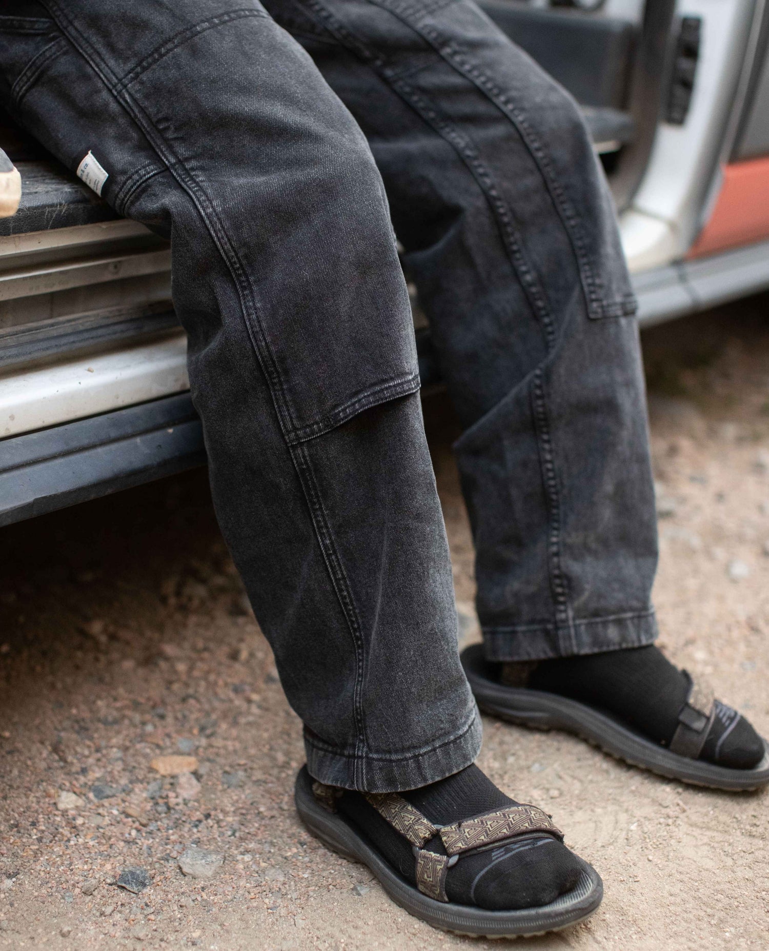 Person wearing black pants and sandals sitting on a vehicle.
