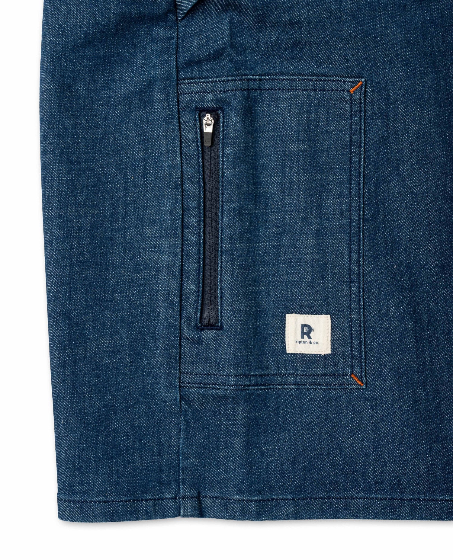 Close-up of a blue denim jacket with a zipper and brand logo on a white background